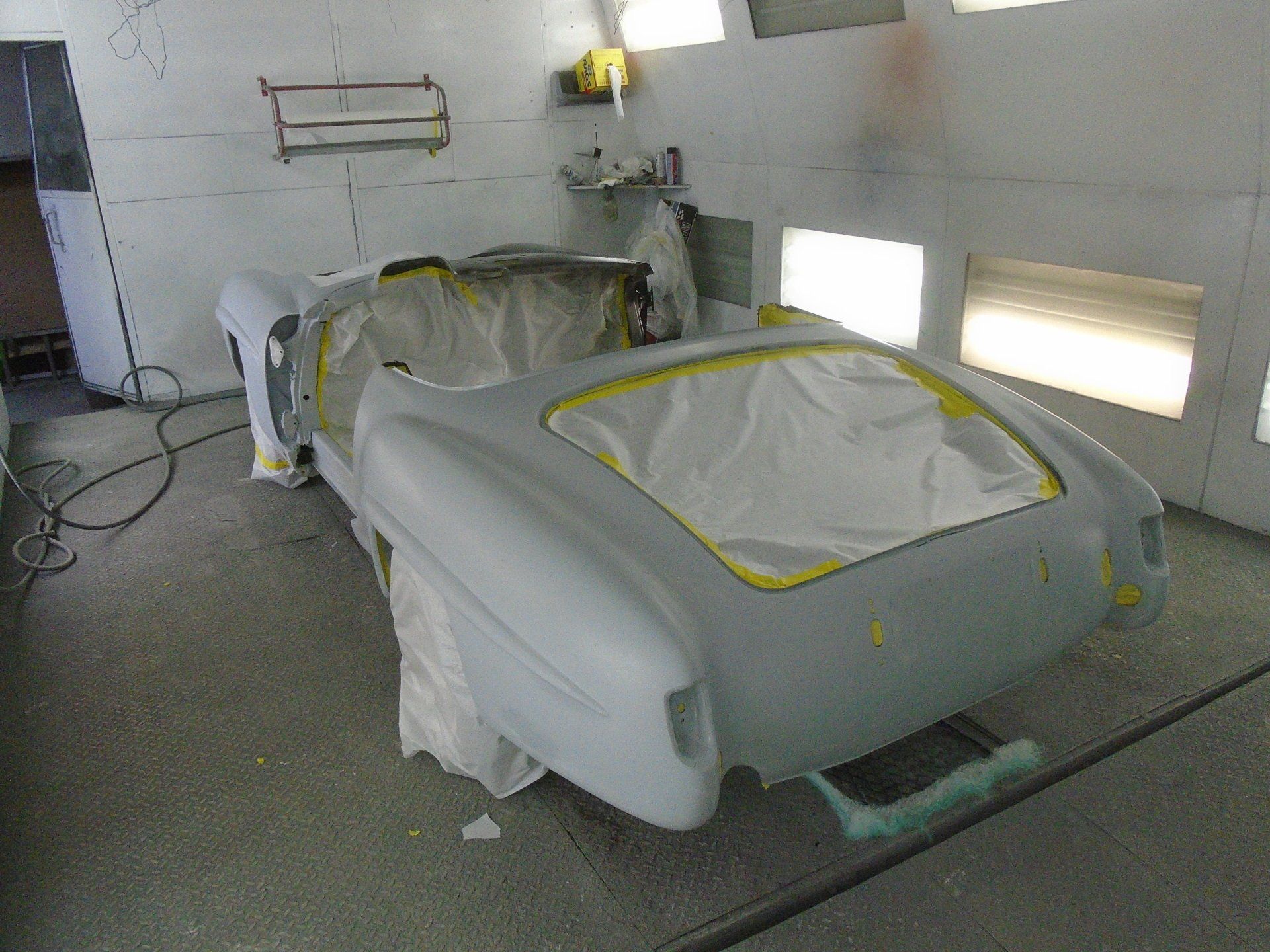 Classic car body in a paint booth, prepared for painting with masking tape and paper.