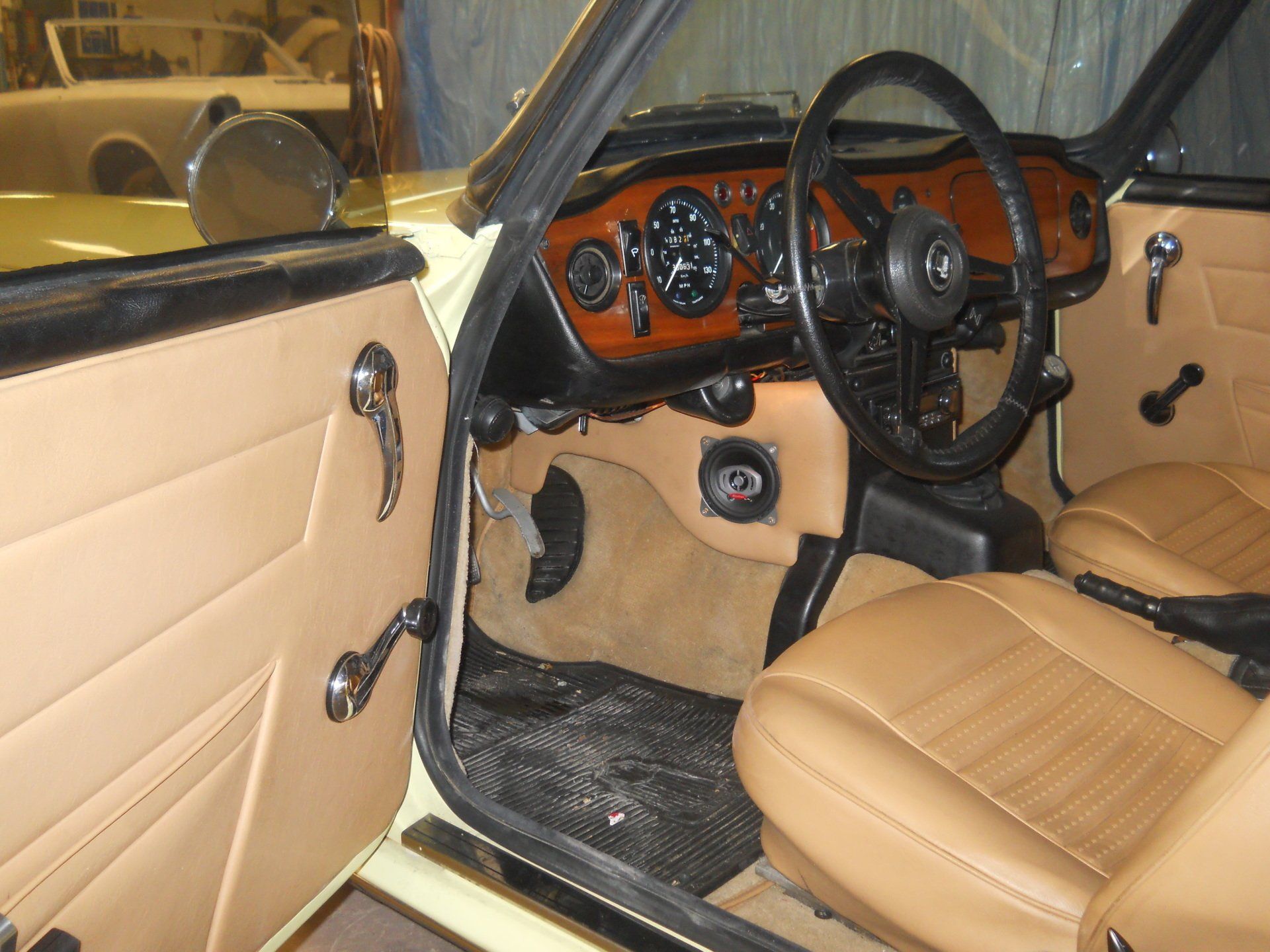 Interior of a classic yellow Triumph sports car with tan seats and wood dashboard.