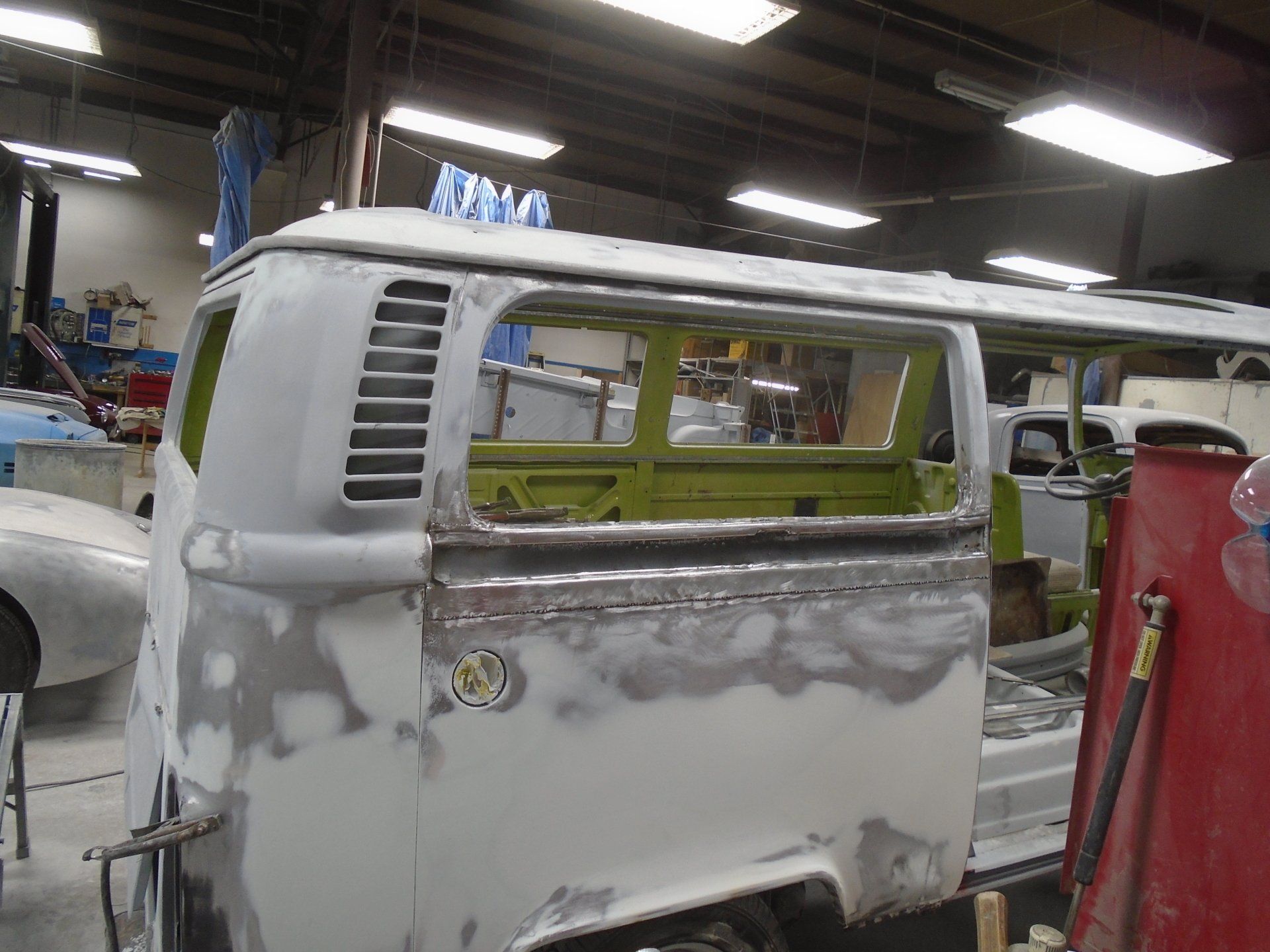 A partially restored gray and green Volkswagen bus in a workshop, metal work visible, preparing for paint.