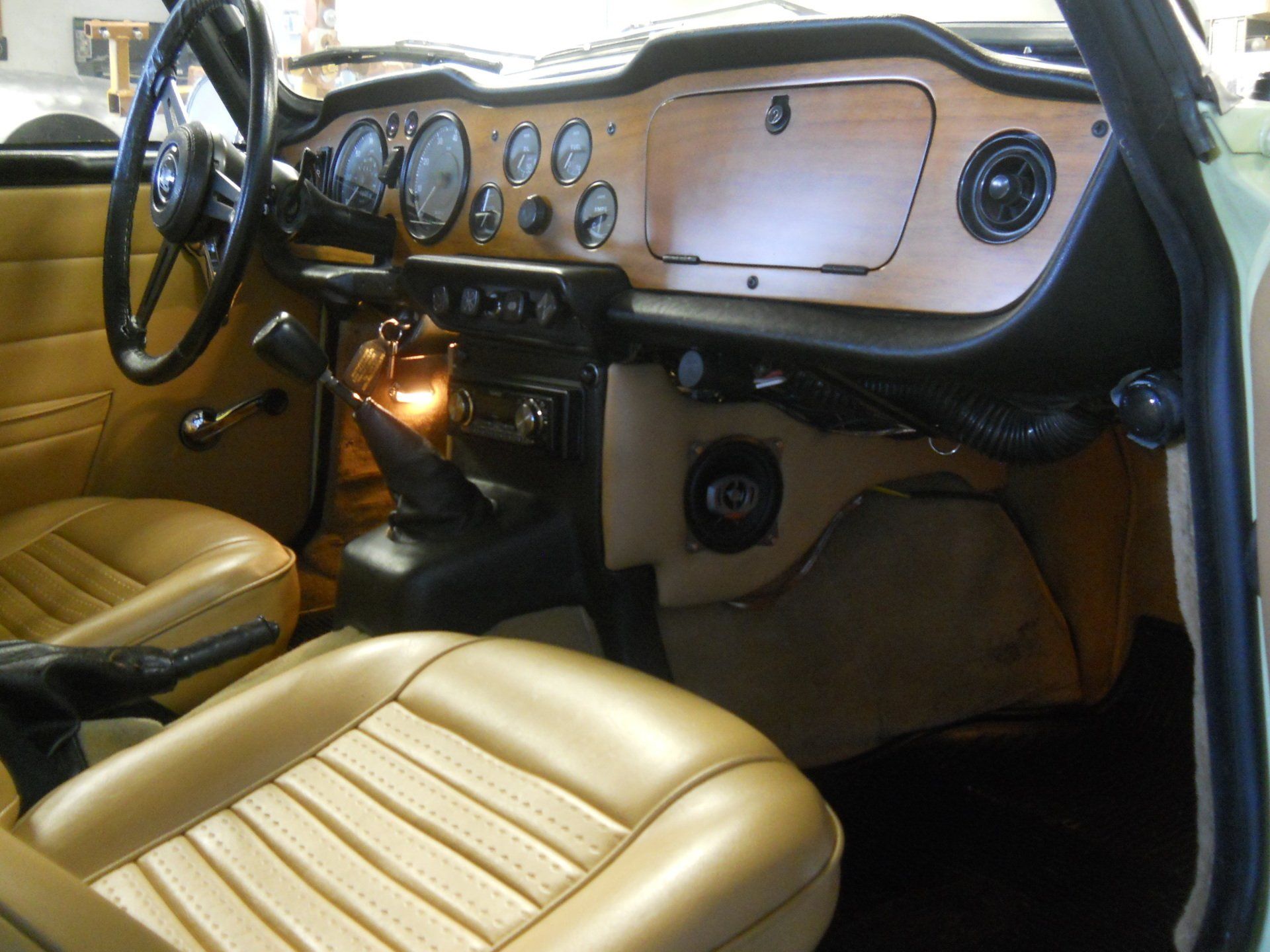 Tan car interior with wooden dashboard, gauges, black steering wheel, and seats.