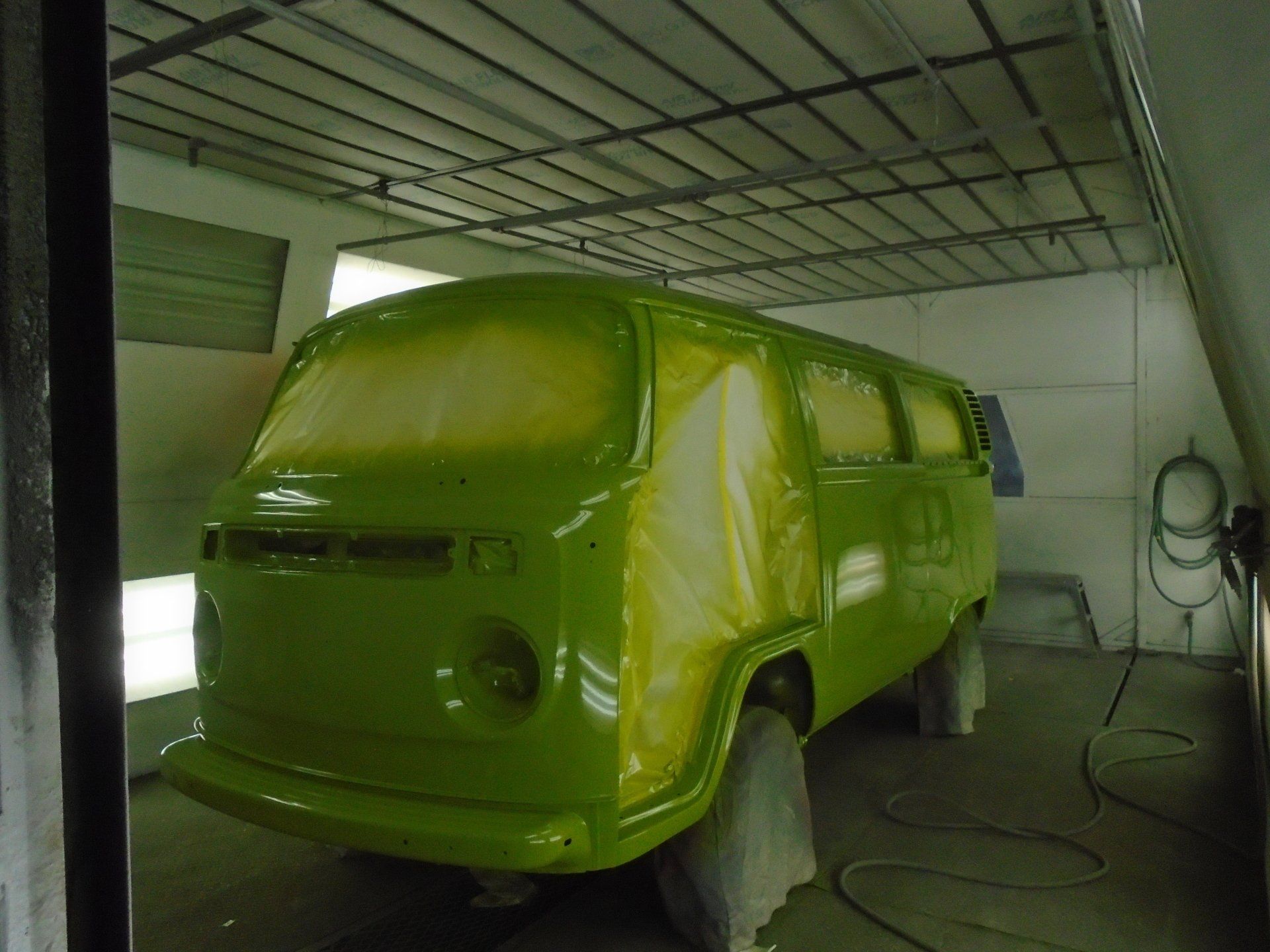 Green Volkswagen van in a spray paint booth, partially painted.