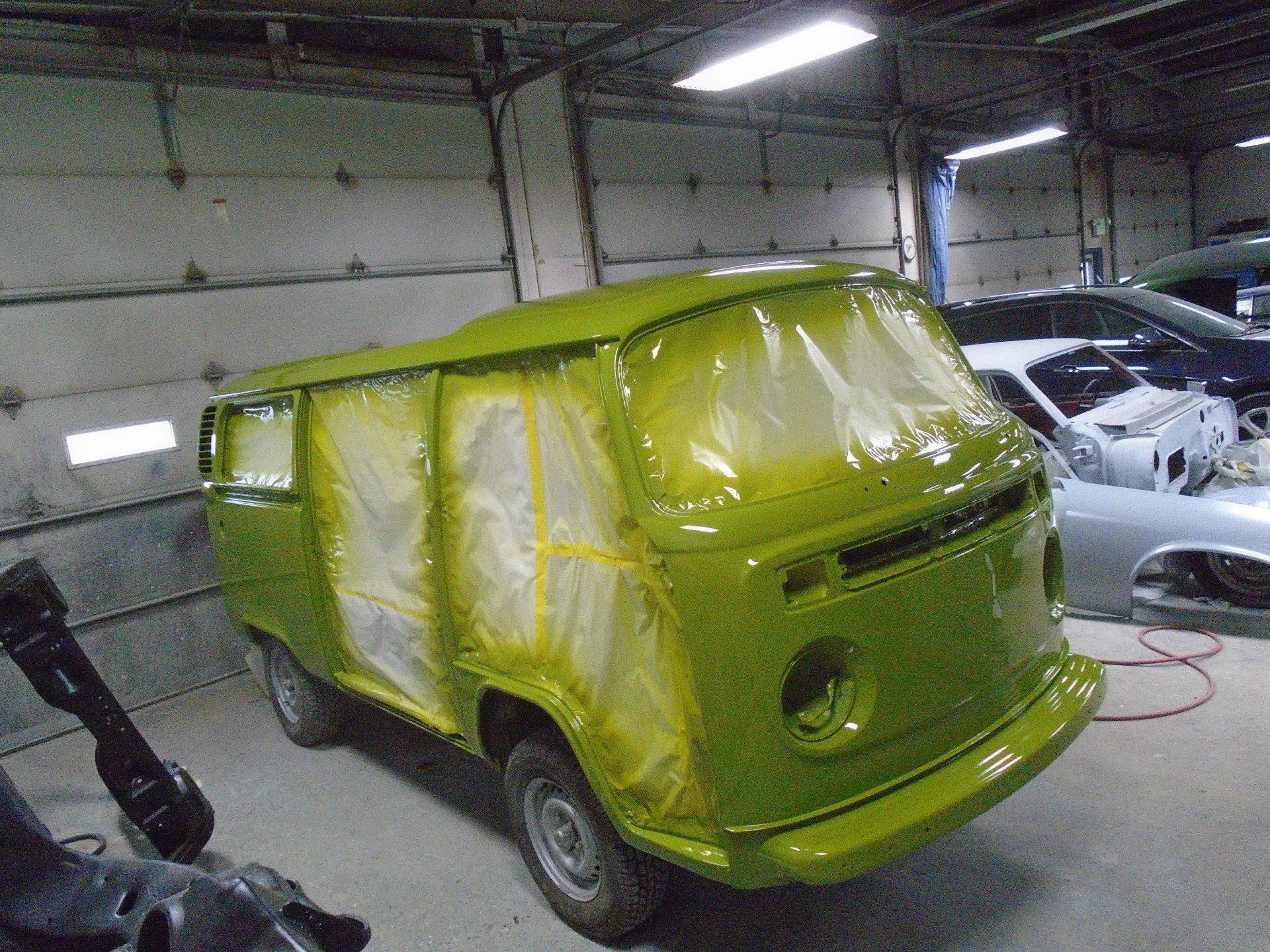 Green vintage van in a garage, taped and covered for painting.