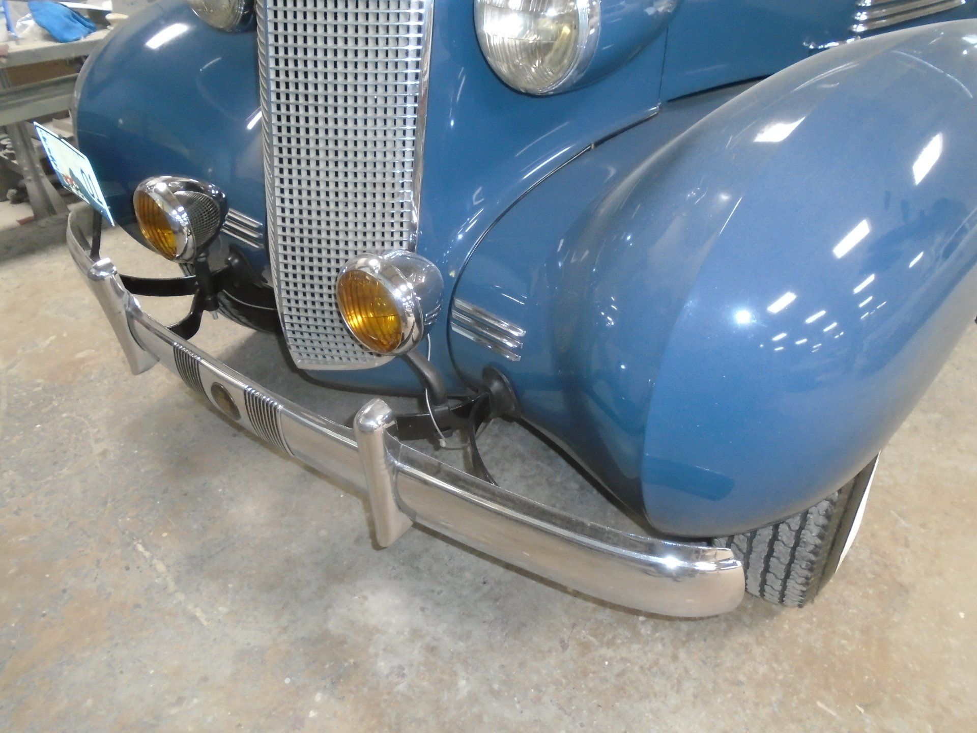 Blue vintage car, chrome bumper, yellow fog lights, silver grille.