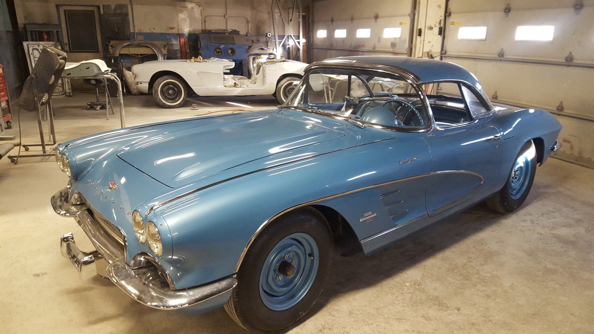 Blue vintage Corvette coupe in a garage, another white Corvette in the background.
