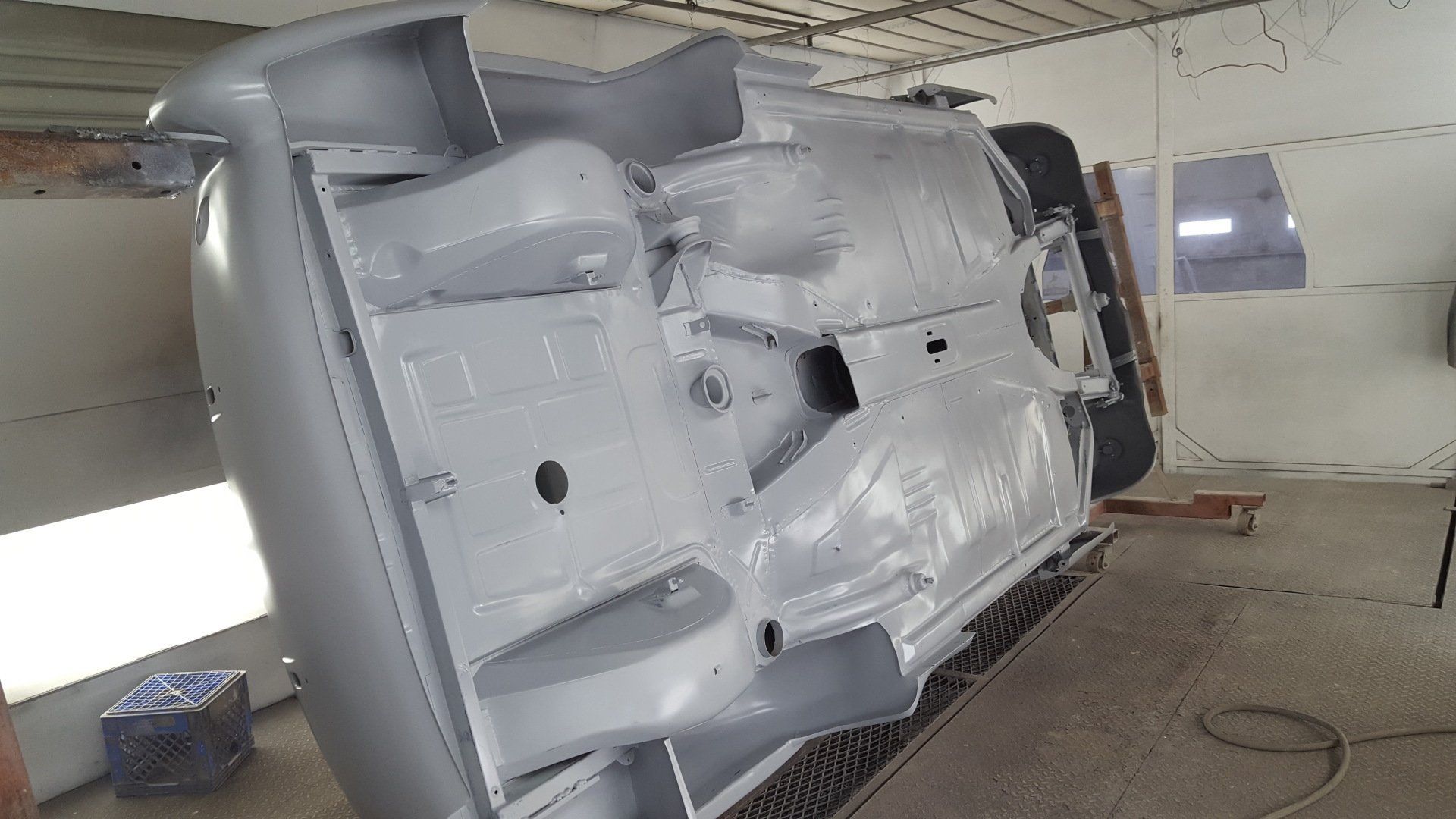 Underside of a classic car chassis, painted gray, in a garage setting.