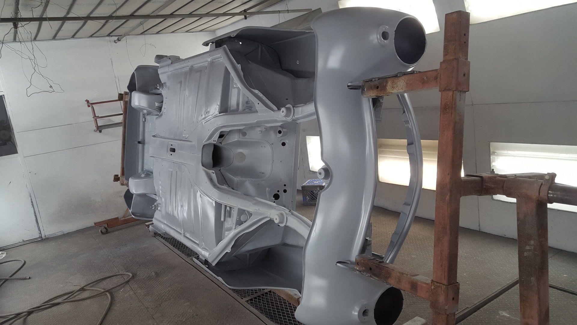 Car chassis, upside down, being painted gray in a workshop.