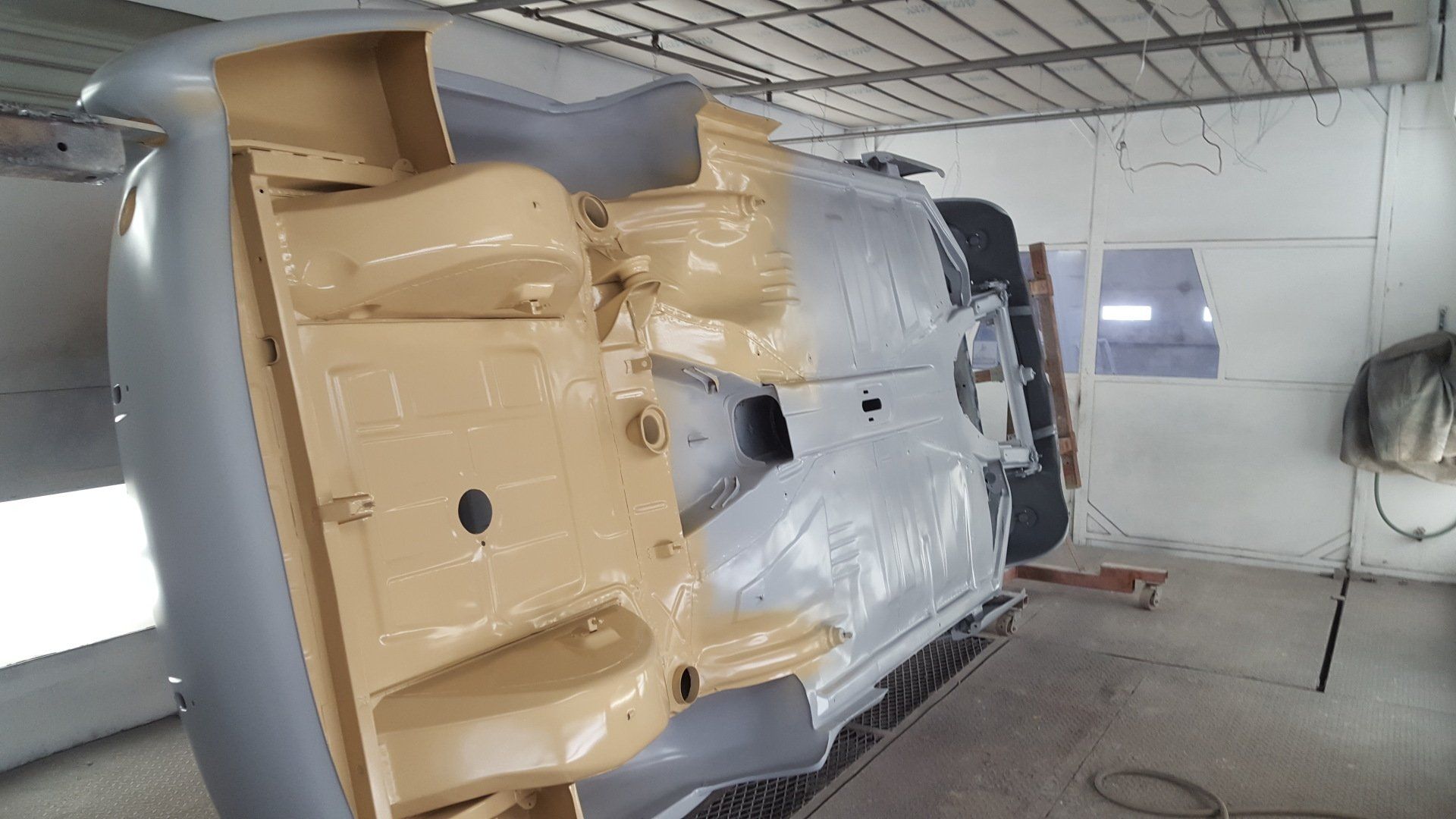 Car chassis being painted in a body shop, showing gray and beige undercoat colors.