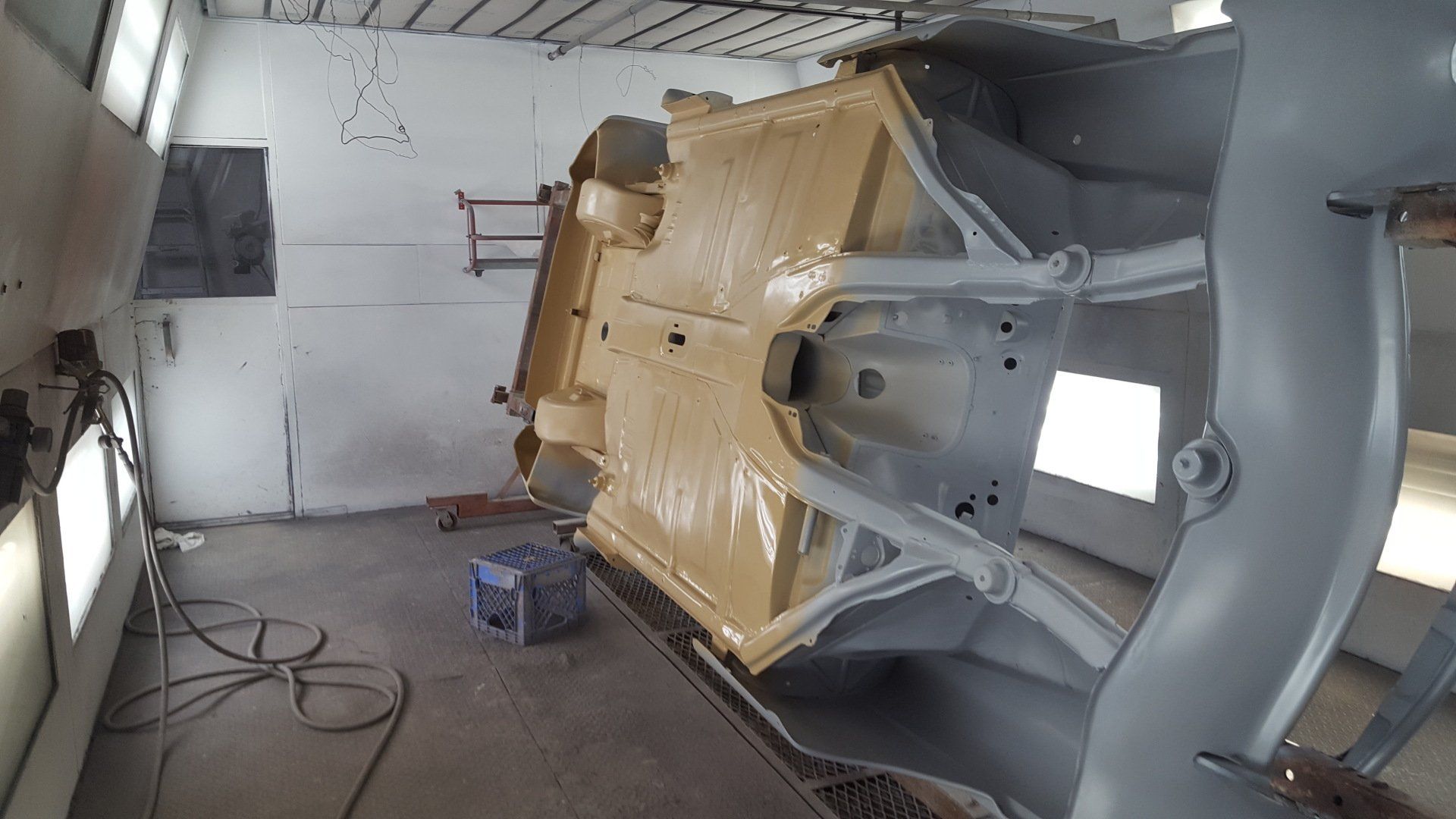 Underside of a car body being painted tan in a spray booth. The frame is light gray.