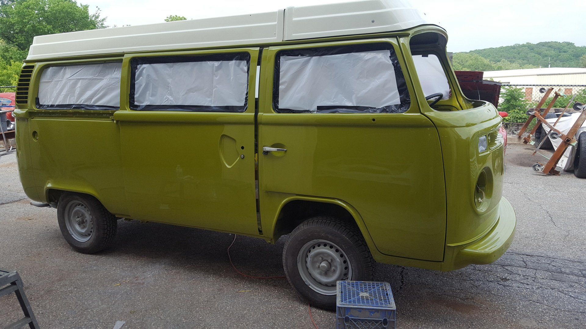 Green Volkswagen camper van with white top, parked outdoors.