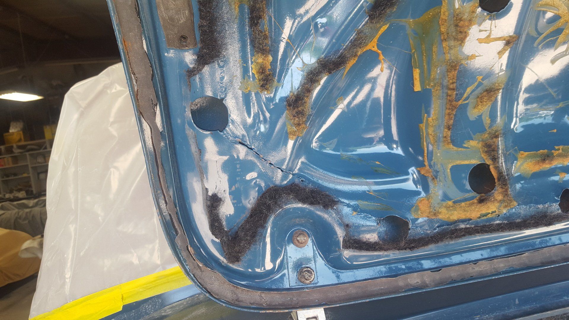 Blue car door interior with black trim, showing corrosion and a crack.