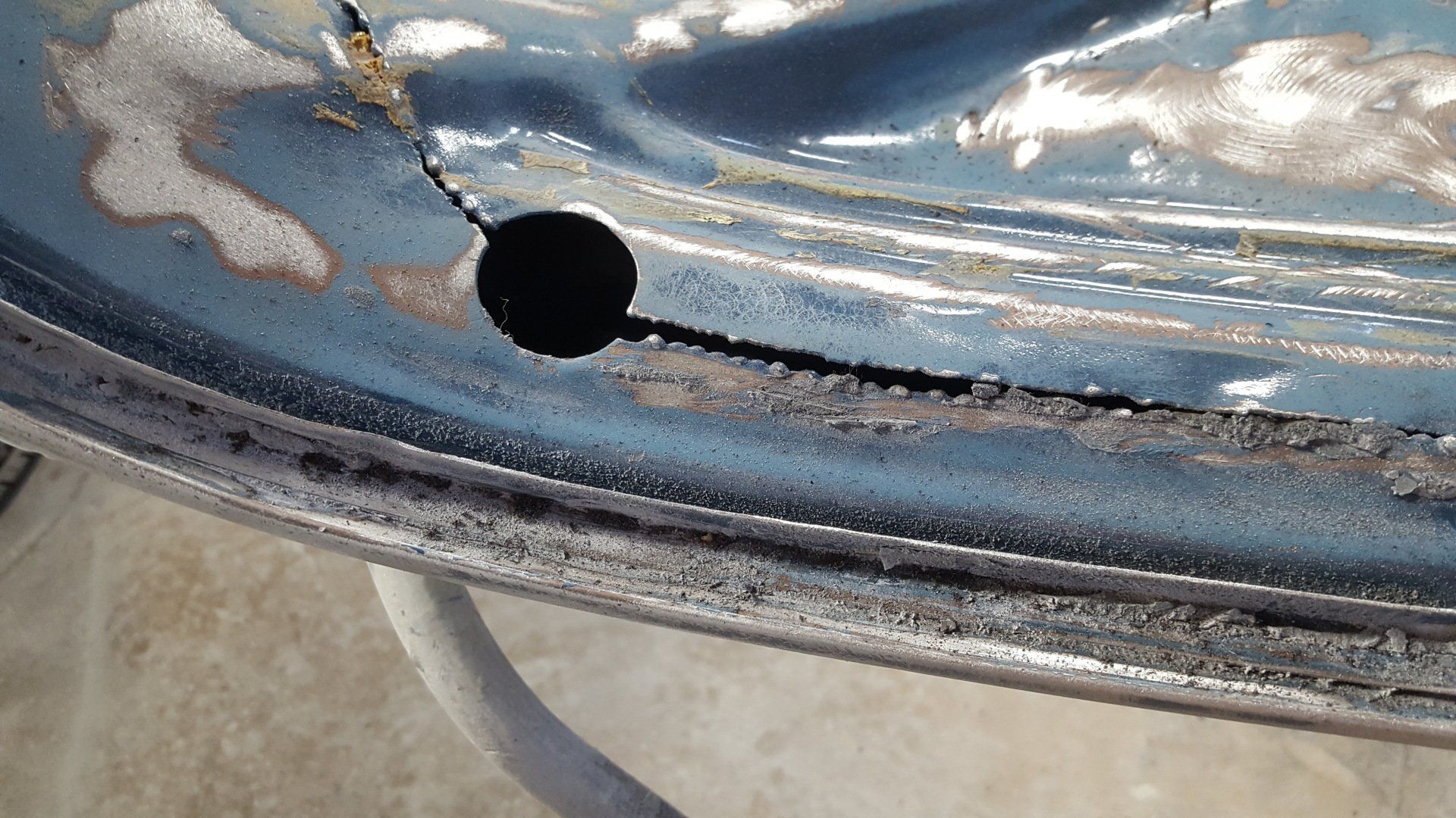 Damaged blue metal wheel rim with a crack, and a hole in it.