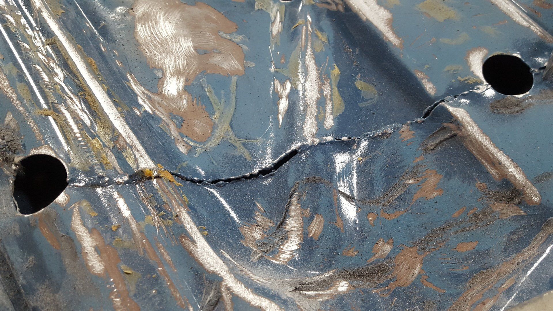 Damaged, blue metal surface with a crack and two circular holes.