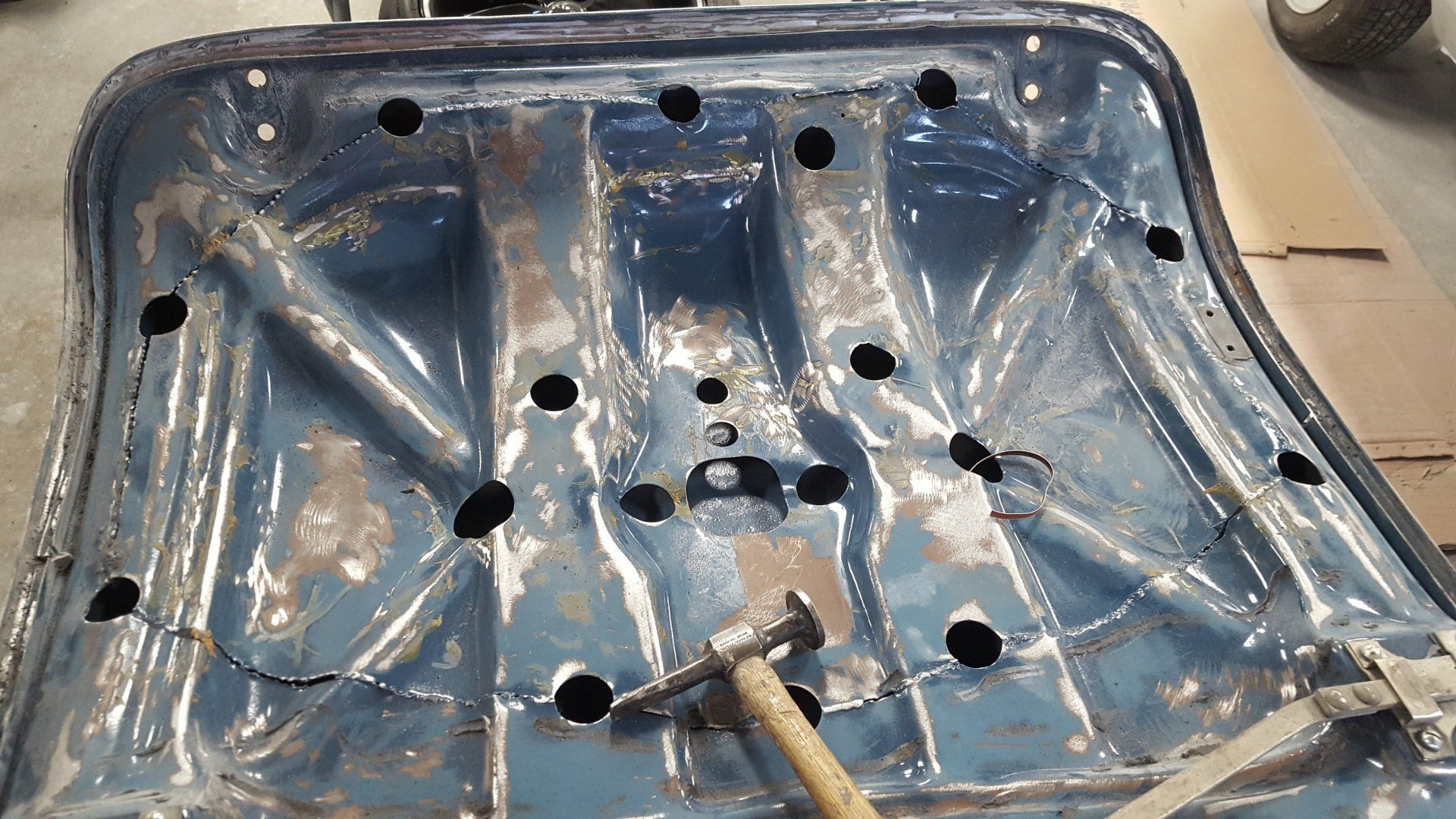 Blue car floor with many drilled holes, a hammer rests inside.