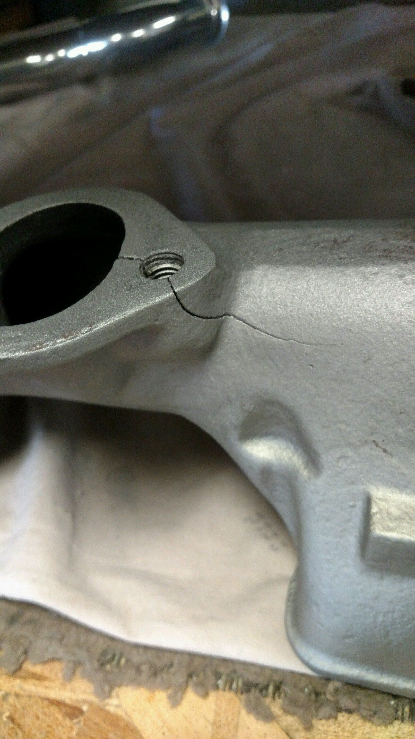 Close-up of a gray metal part with a crack extending from a bolt hole.