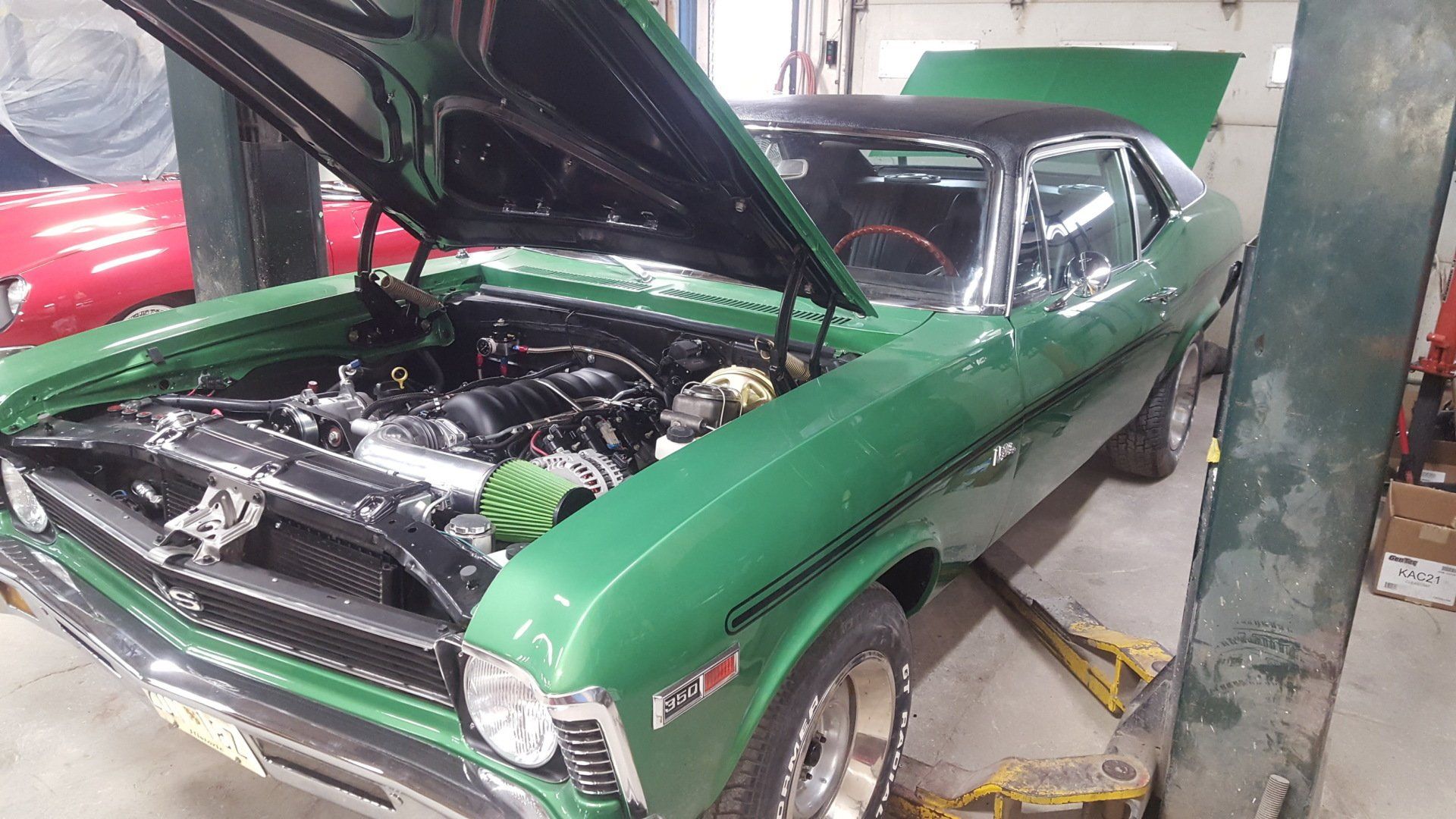 Green classic car with black roof, hood open, parked in a garage.