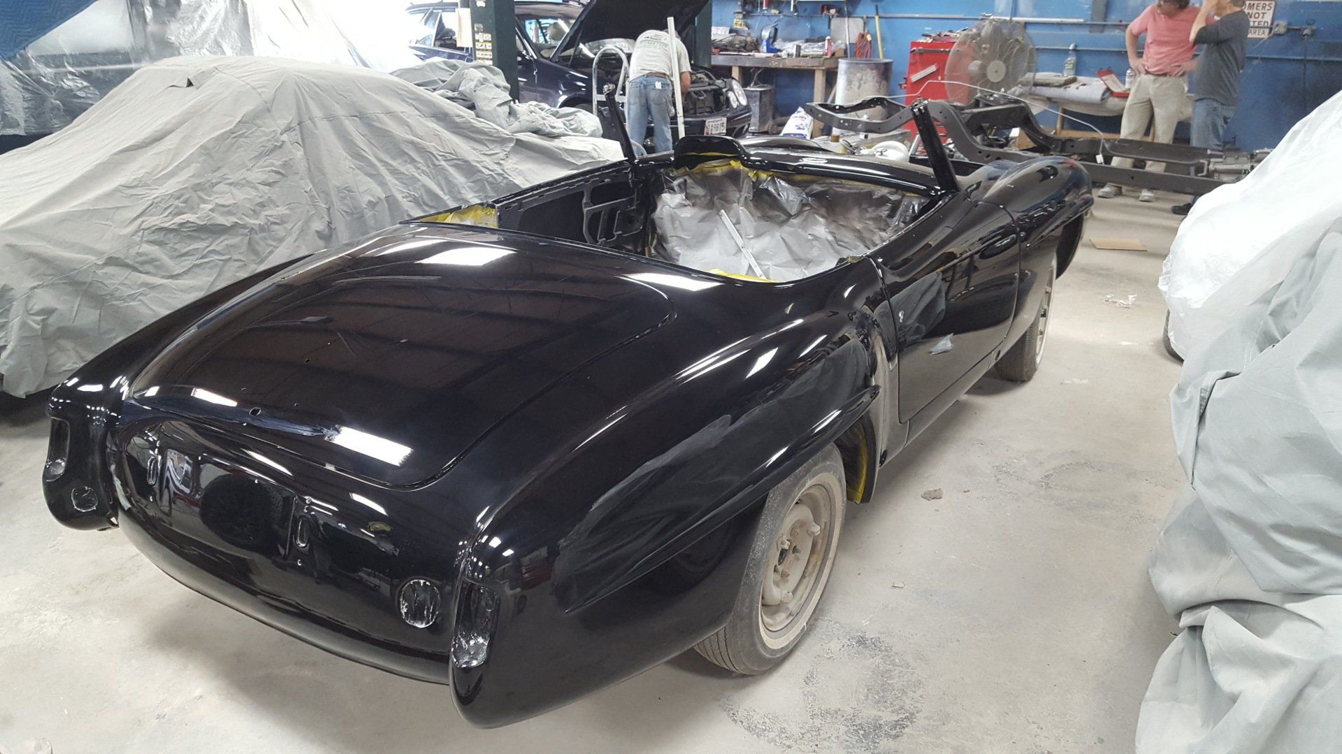 Black convertible car in a workshop, partially restored.