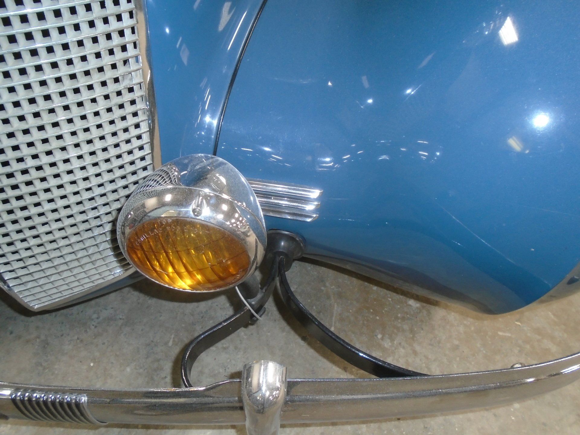 Blue vintage car with chrome headlight and grill.