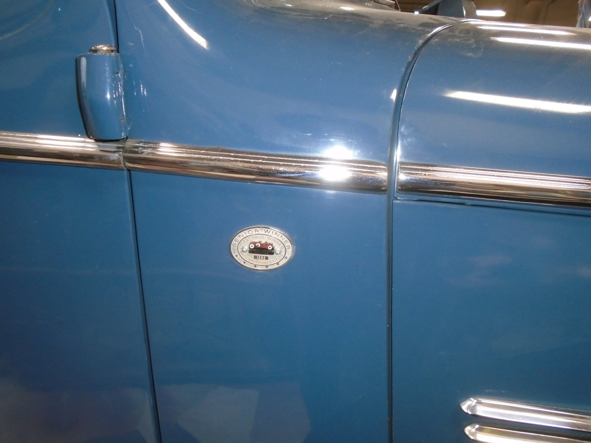 Blue car door with a circular emblem and chrome trim.