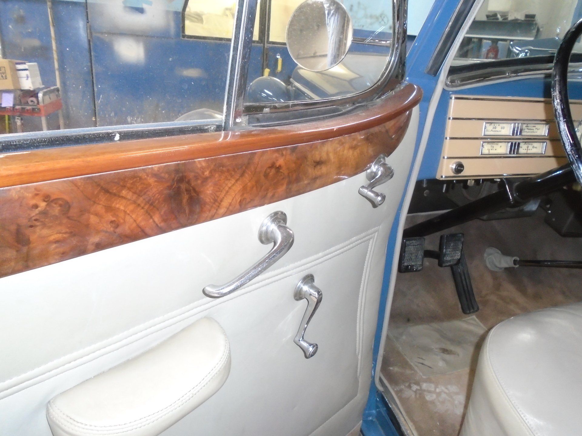 Interior car door with wood trim, cream paneling, and chrome handles.