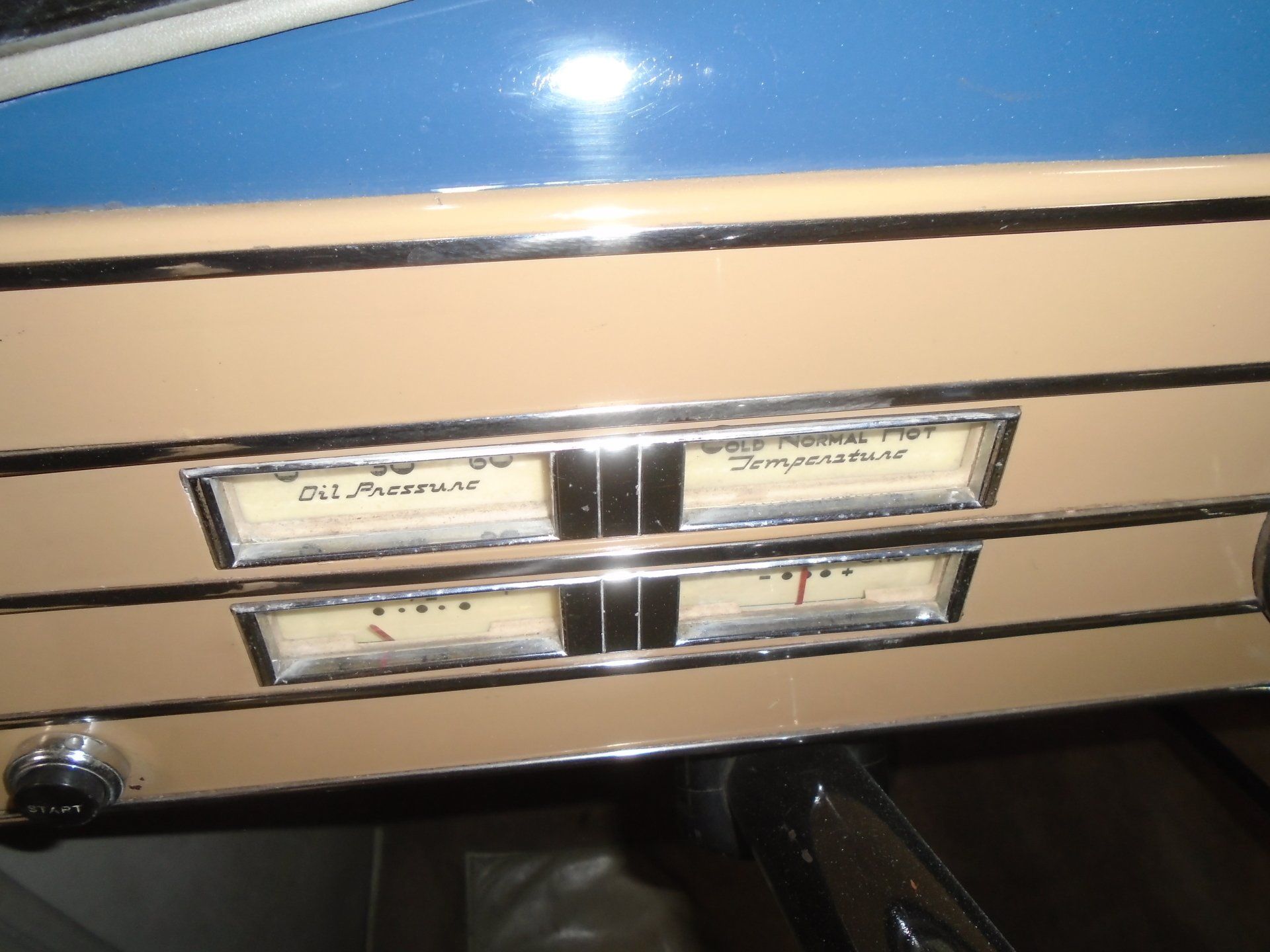 Close-up of a vintage car dashboard with gauges for oil pressure and temperature, in a tan and chrome finish.