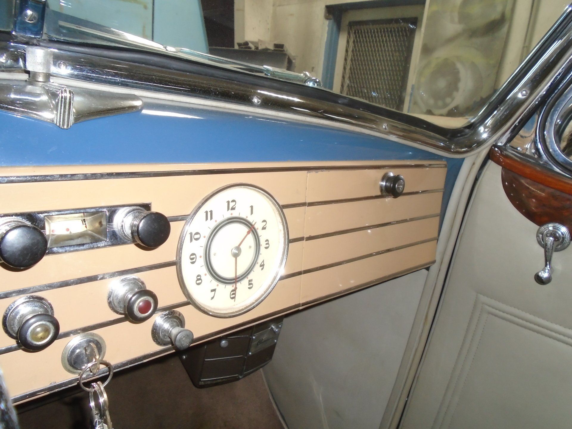 Interior of a vintage car dashboard with a tan and blue color scheme, clock, and chrome accents.