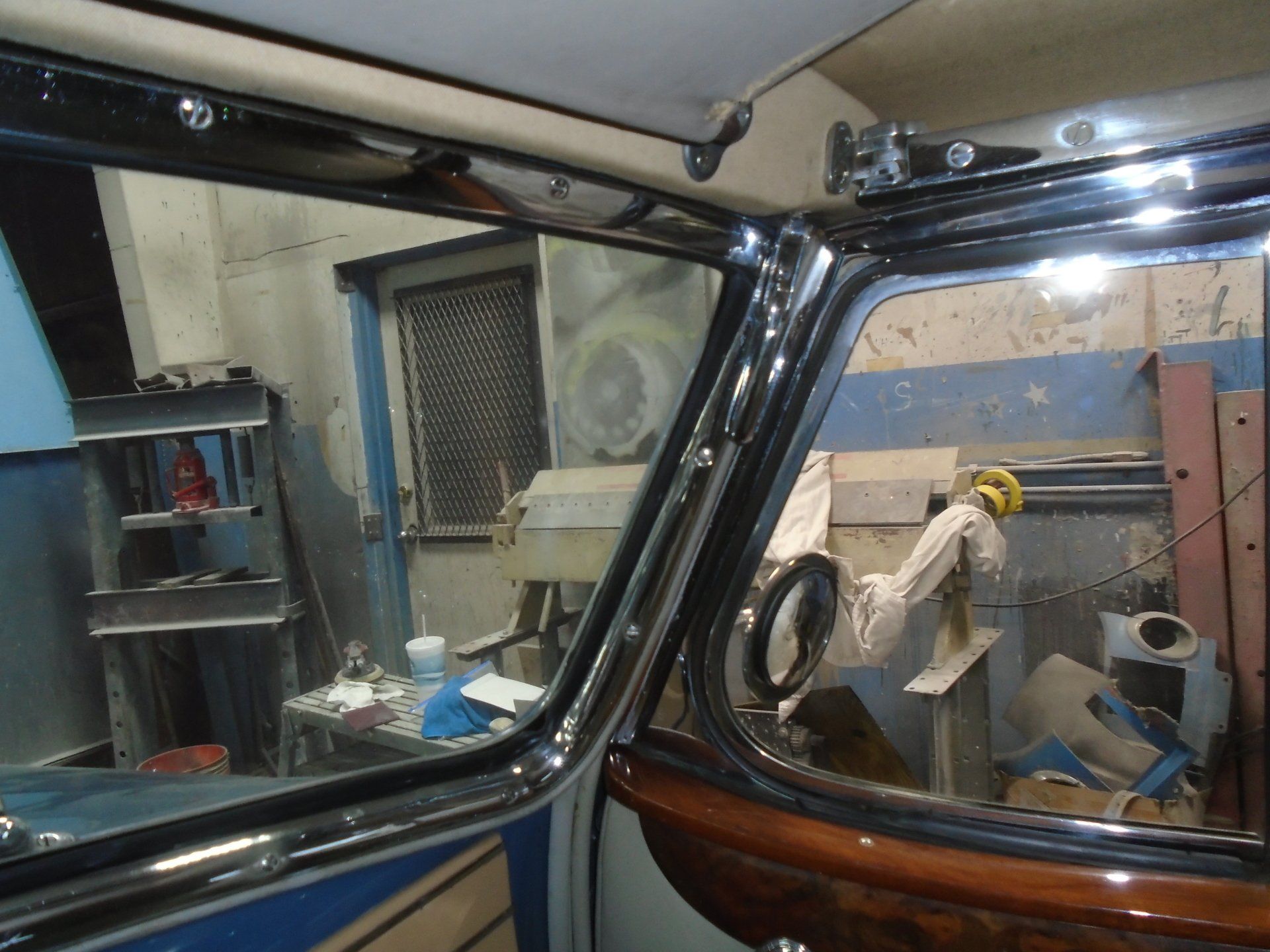 Interior of a classic car, showing chrome trim and windows, with tools and a work area visible in the background.