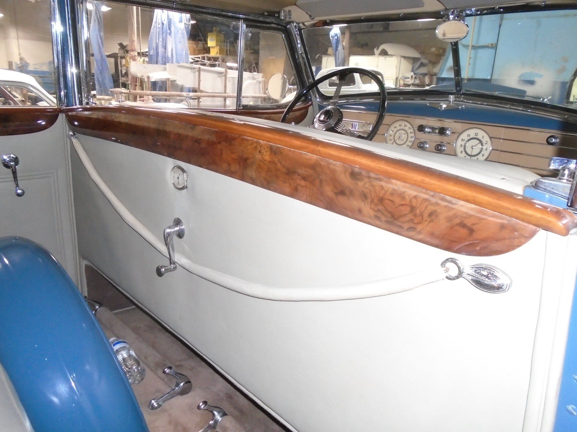 Interior of a vintage car with wood trim, white paneling, and a black steering wheel.