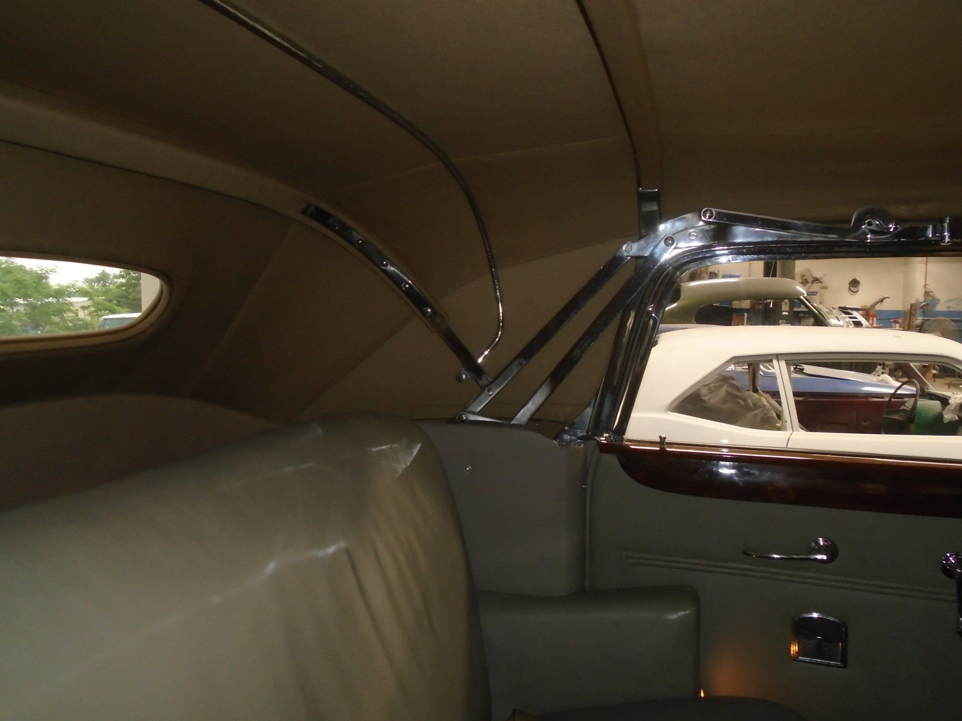 Interior view of a classic car with tan upholstery and chrome accents. Another car is visible through the open door.
