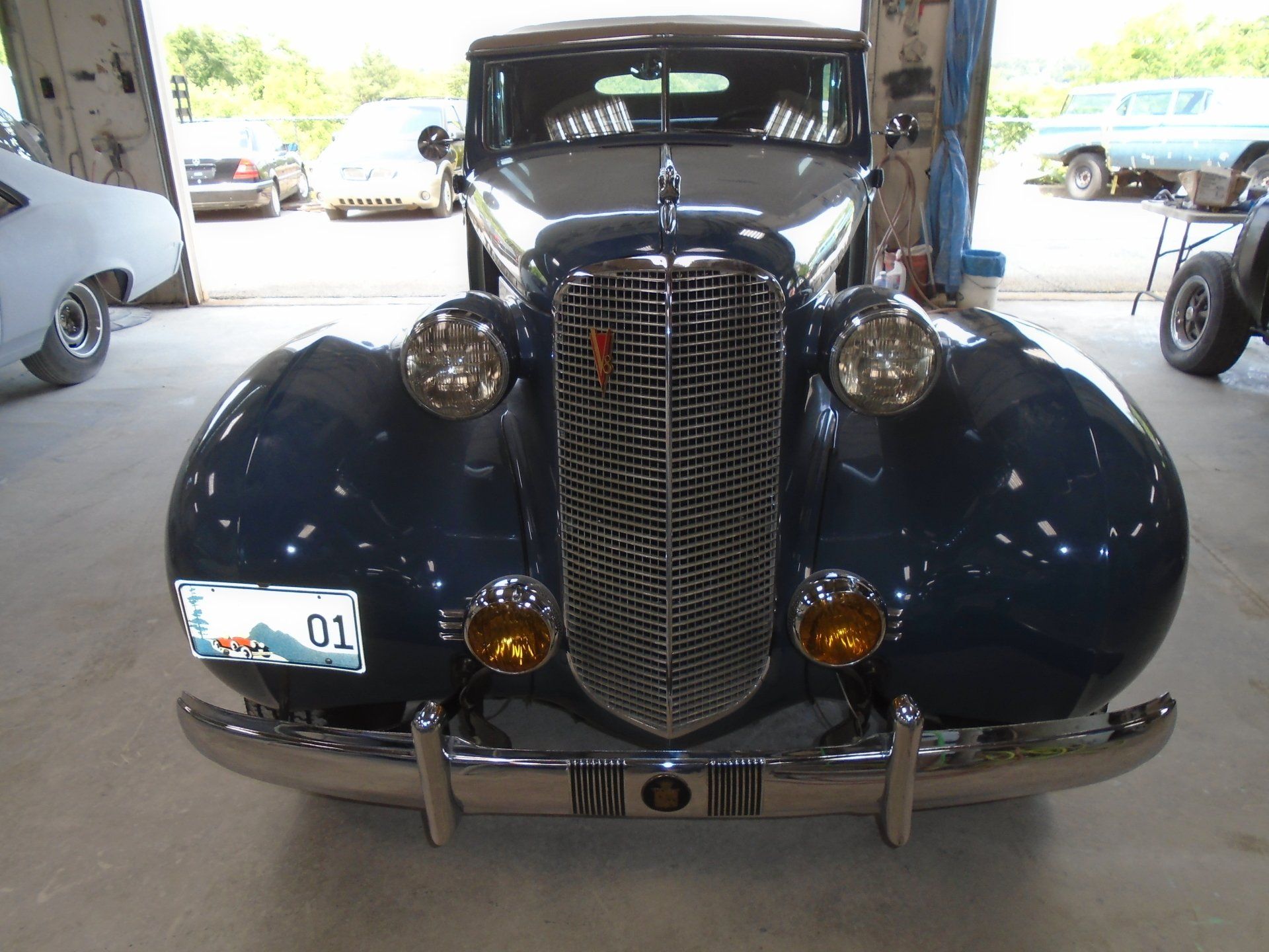 Dark blue vintage car, chrome grill and bumpers, inside a garage.