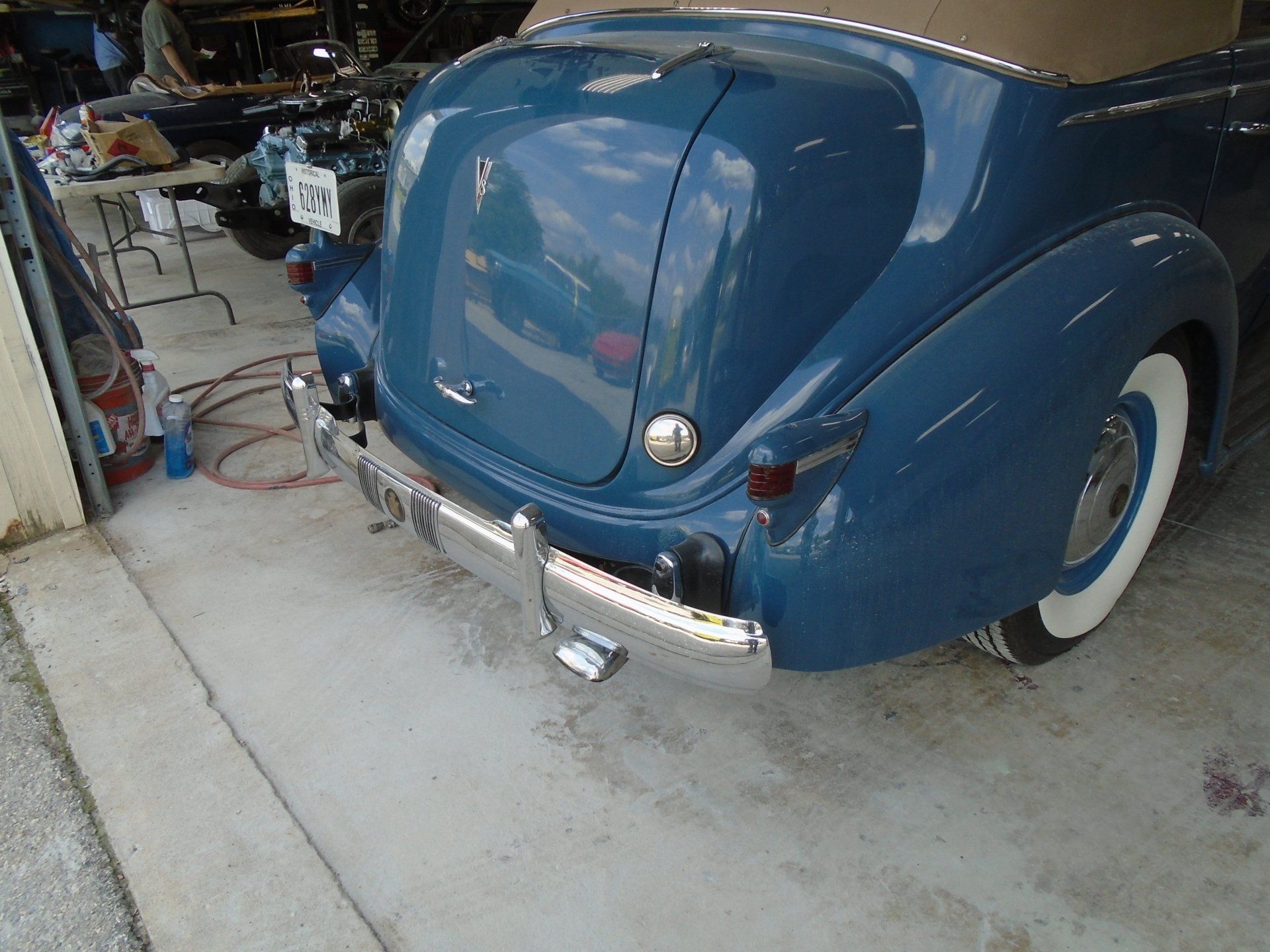 Blue classic car, rear view, white-wall tires, chrome bumper, light tan convertible top.