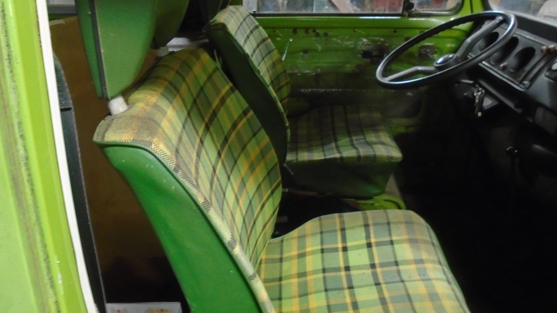 Green plaid seats inside a green vintage van. Steering wheel and dash are visible.