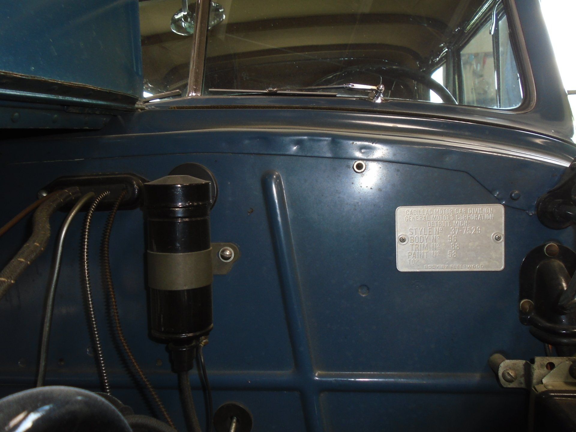 Blue dashboard of a classic car with a black ignition coil and metal plate.