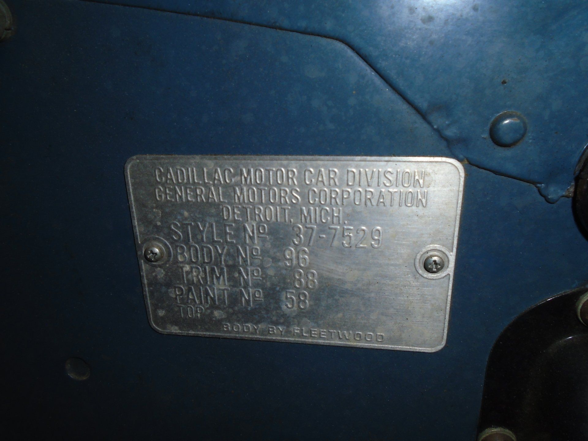 Cadillac data plate, silver on blue car door, with text: style, body, trim, and paint codes.