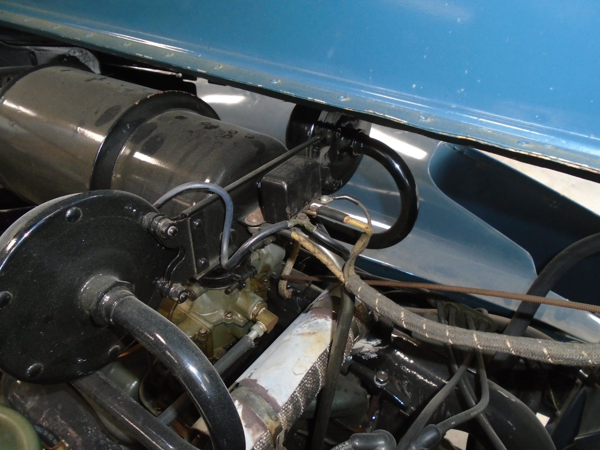 Car engine components: black cylinders, hoses, and silver tube, against a blue car frame.