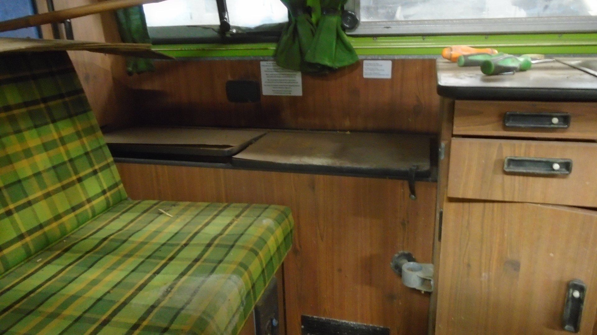 Interior of a vintage van with plaid seat, wooden cabinetry, and a small countertop, with tools.