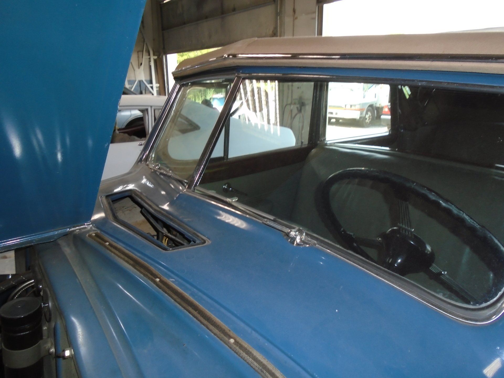 Blue classic car, open hood, showing interior with steering wheel and windows.