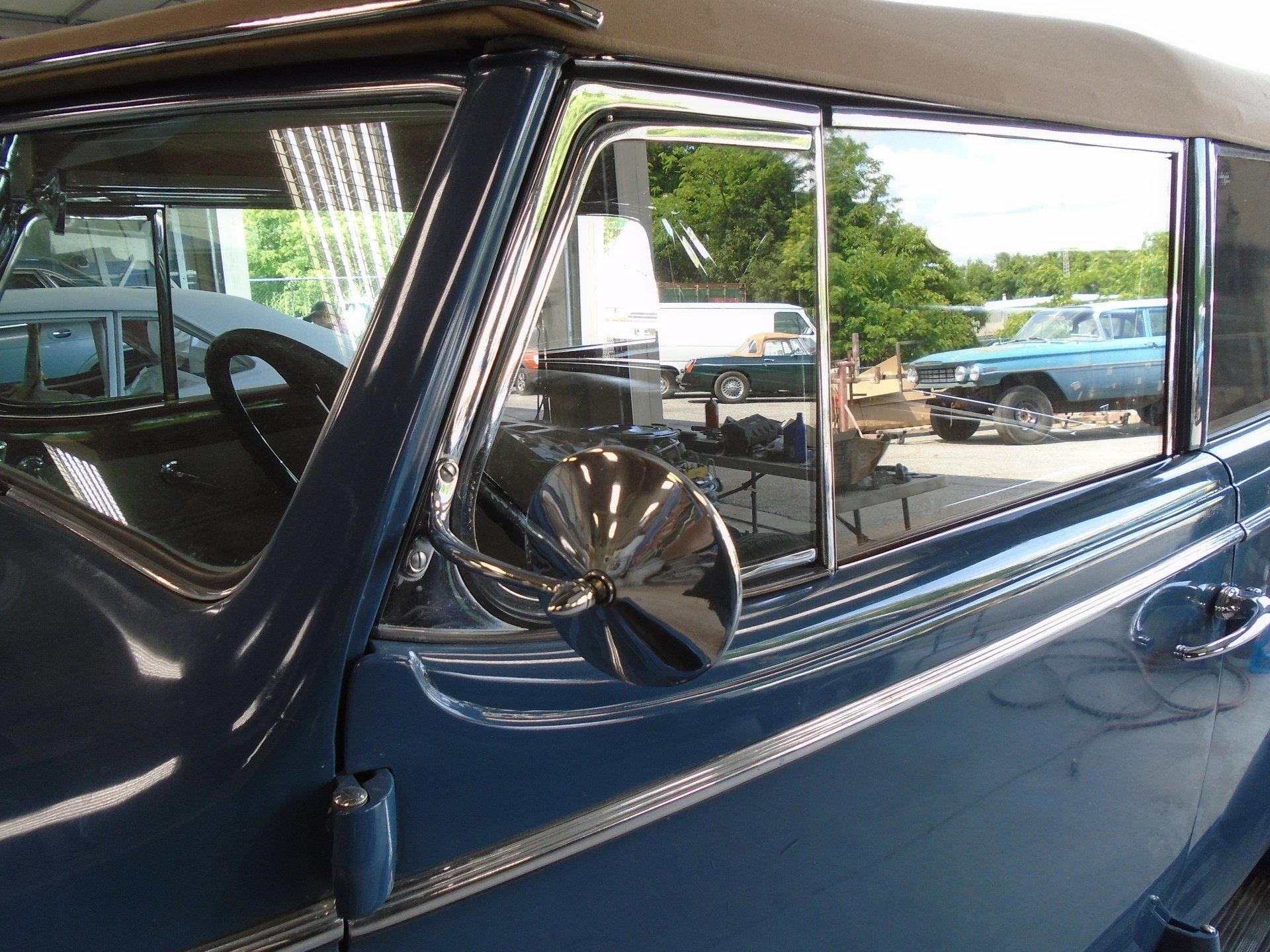 Blue vintage car door with chrome mirror, reflecting a sunny outdoor scene.