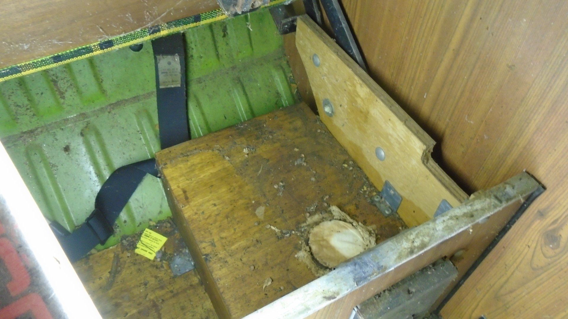 Wooden box in vehicle storage area, partially open. Green, brown, and metal components visible.