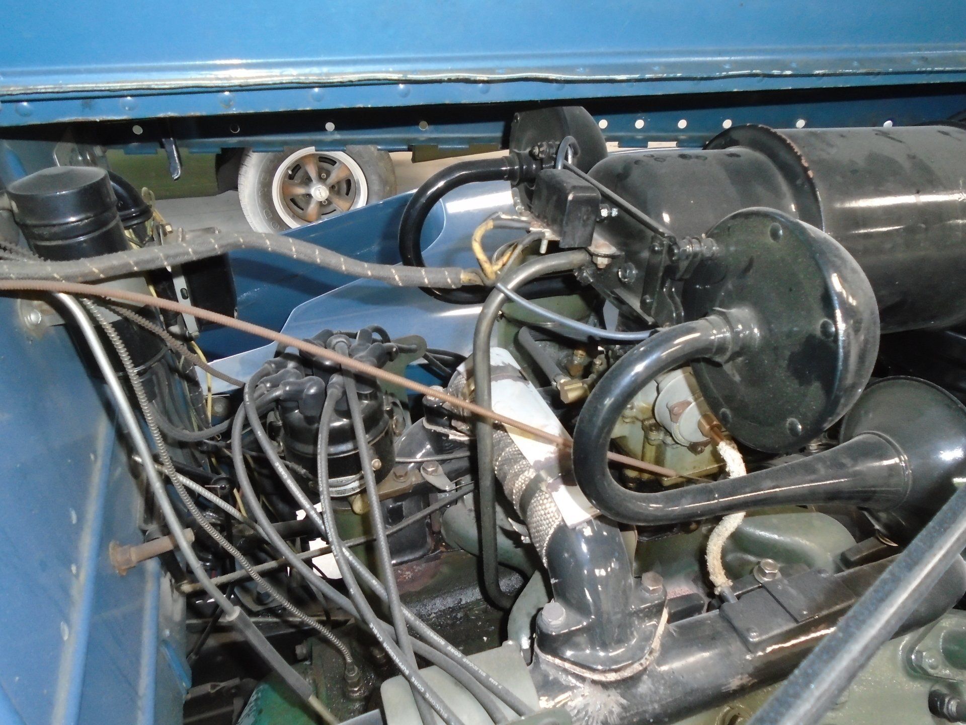 Engine compartment of a blue vehicle. Black engine, wiring, and horns are visible.
