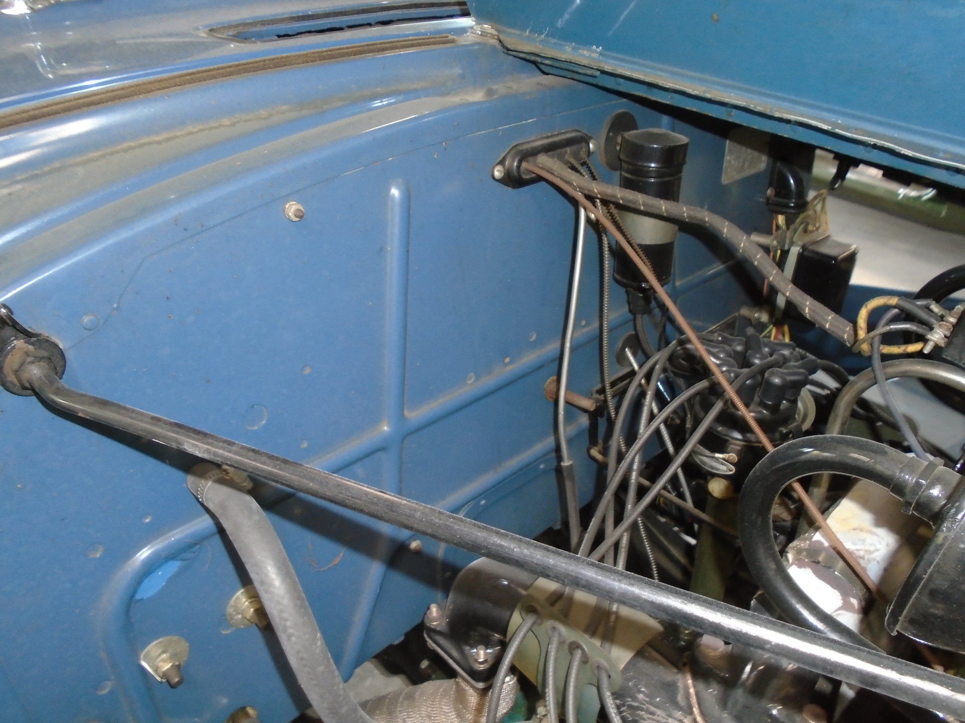 Blue car engine compartment, various components visible including brake lines and support bar.