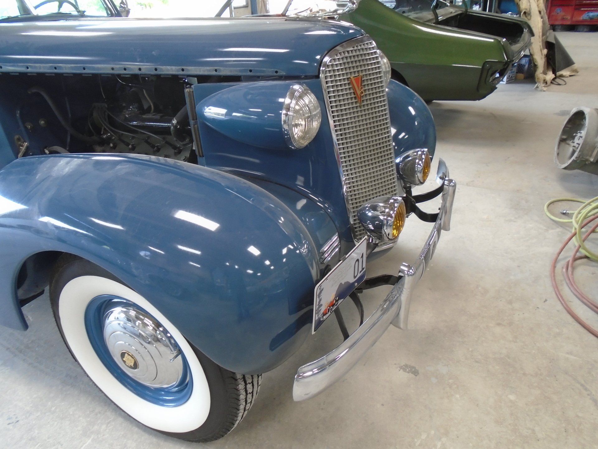 Blue vintage car with chrome grille and white-walled tires in a garage setting.