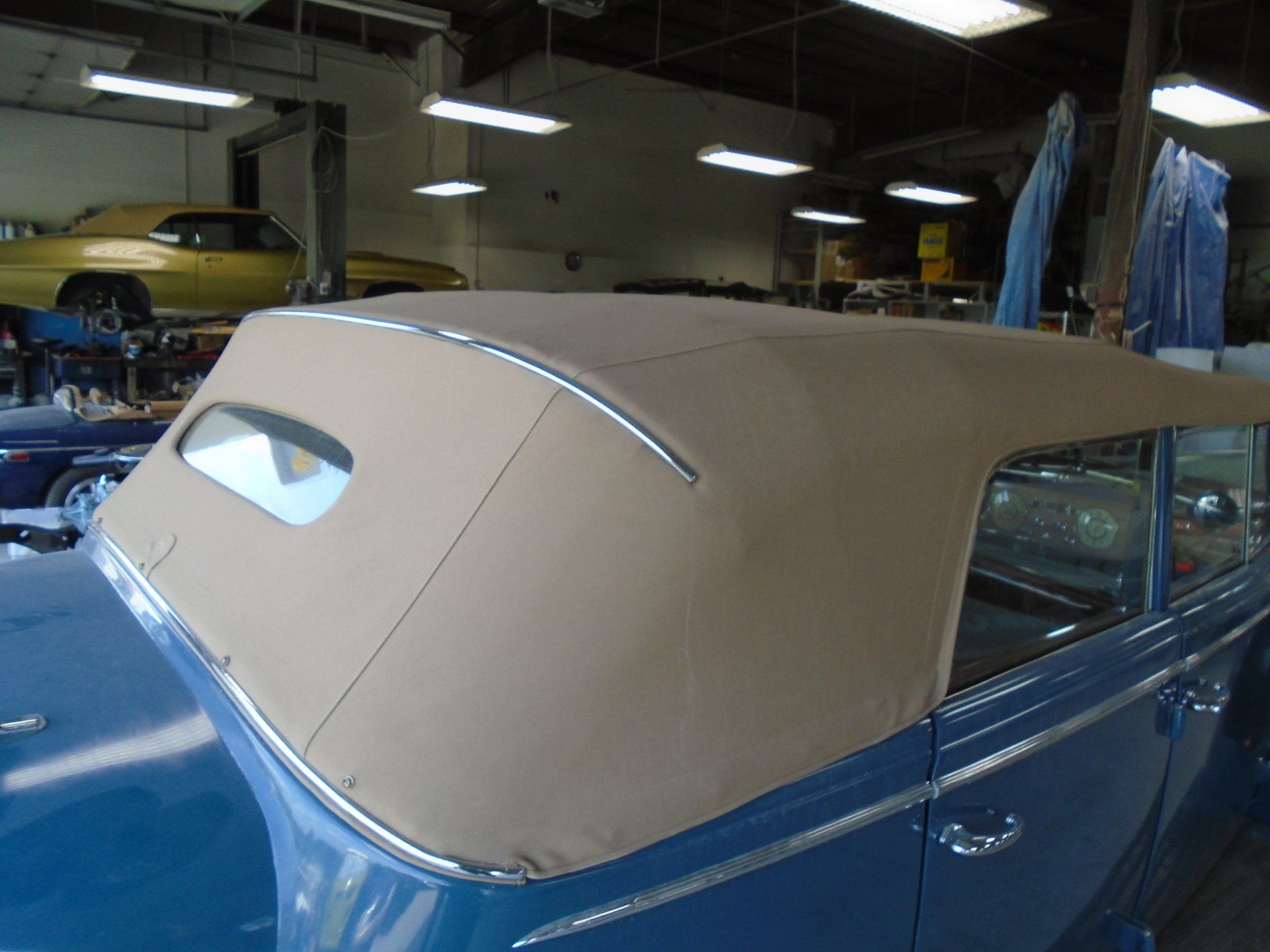 Blue vintage car with tan convertible top in a garage.