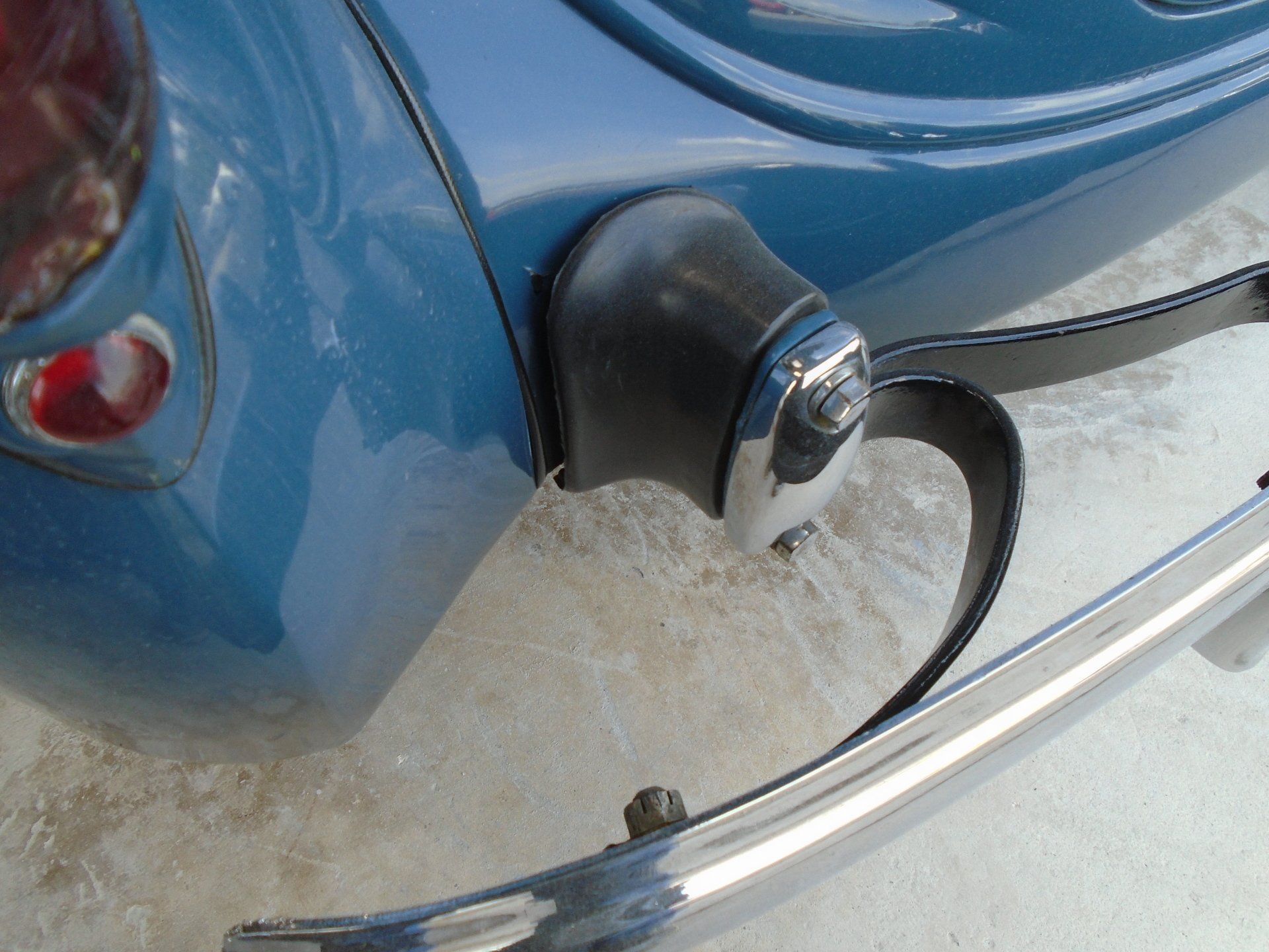Blue car corner with chrome bumper, black rubber bumper guard, and tail light.