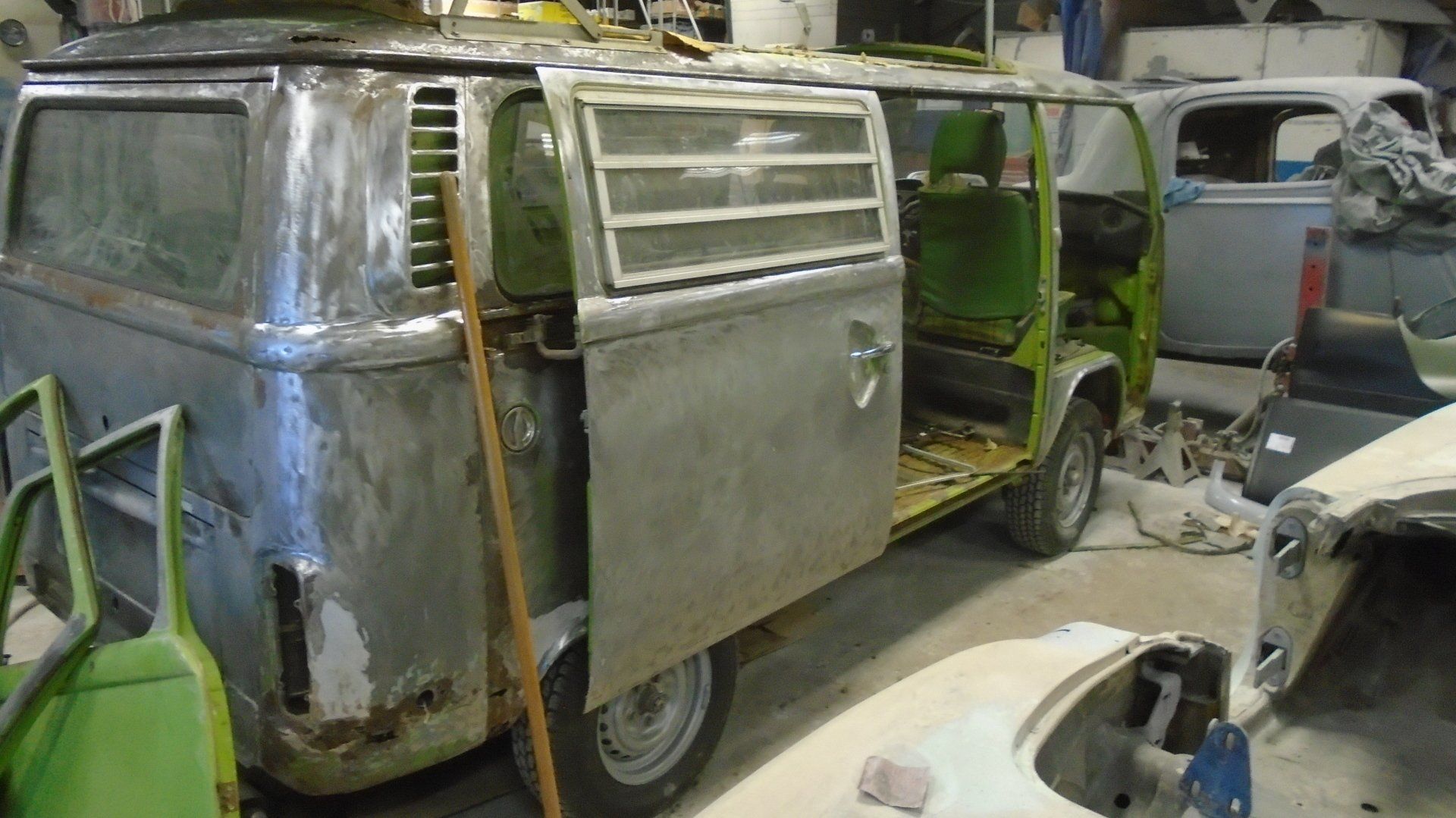 A partially disassembled, silver and green vintage Volkswagen bus in a workshop, undergoing restoration.
