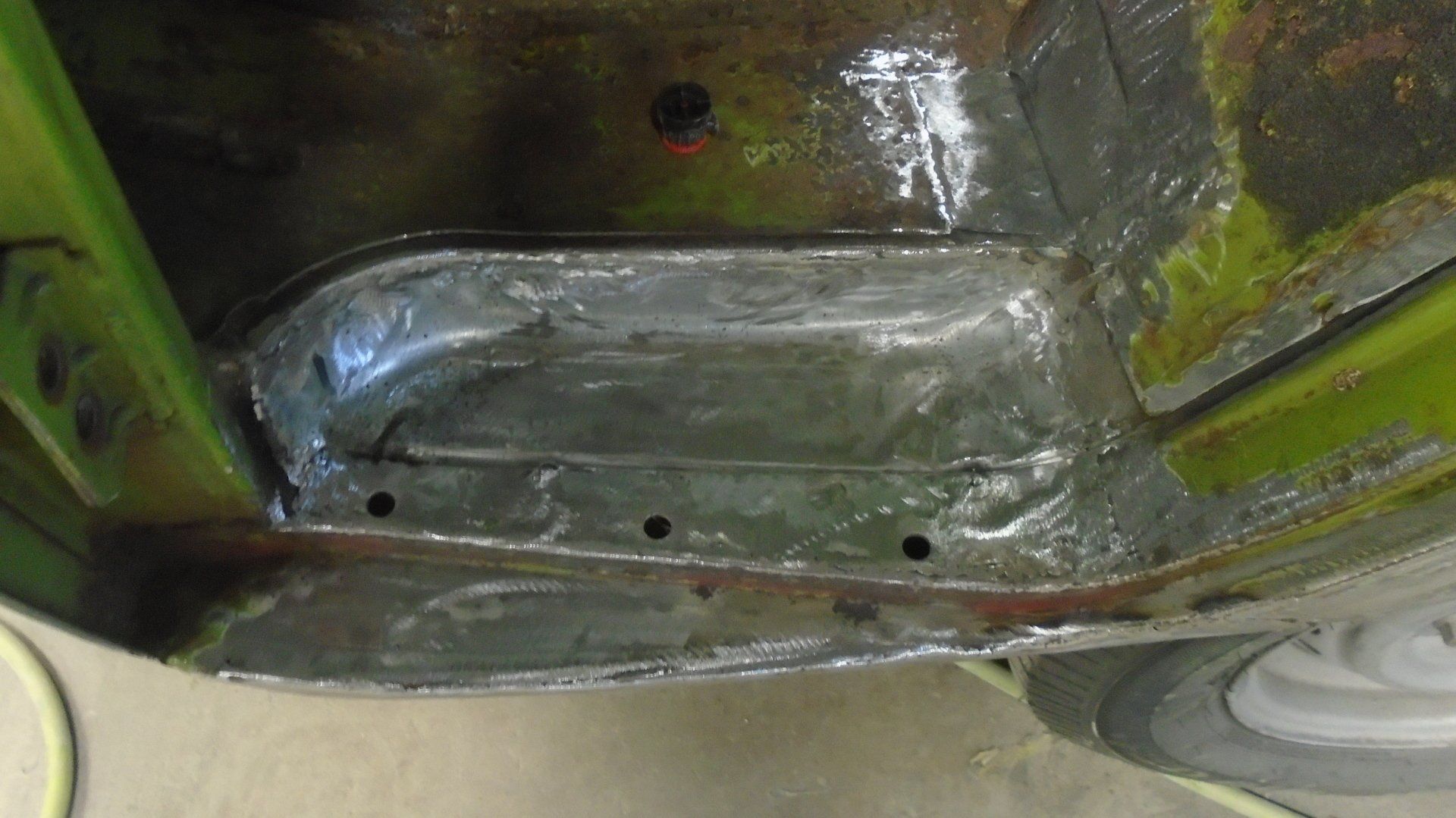 Inner car panel showing a rusted and repaired section, featuring welding marks and bolt holes.