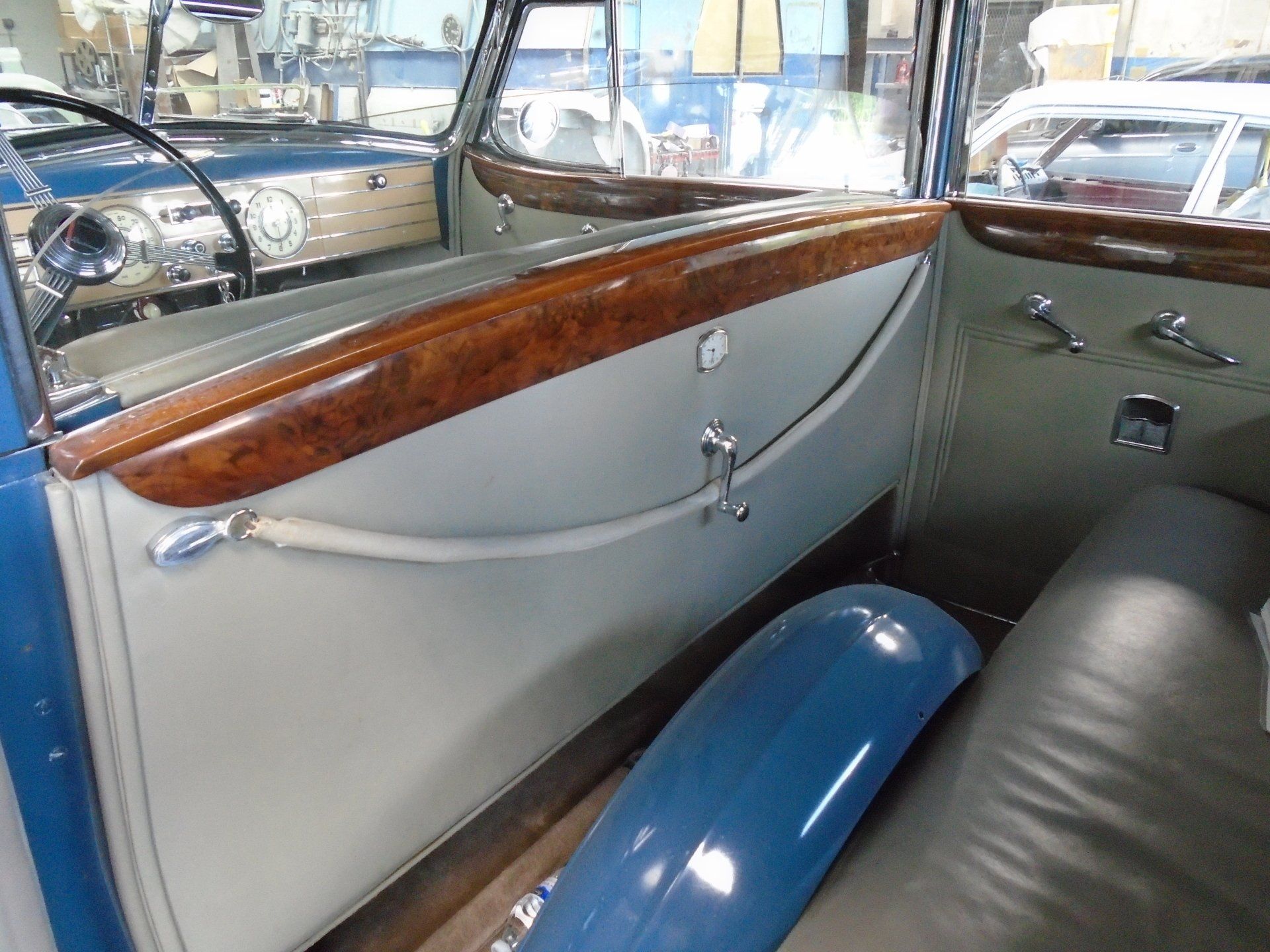 Interior of a vintage blue car, showing the door panel with wooden trim and tan leather.