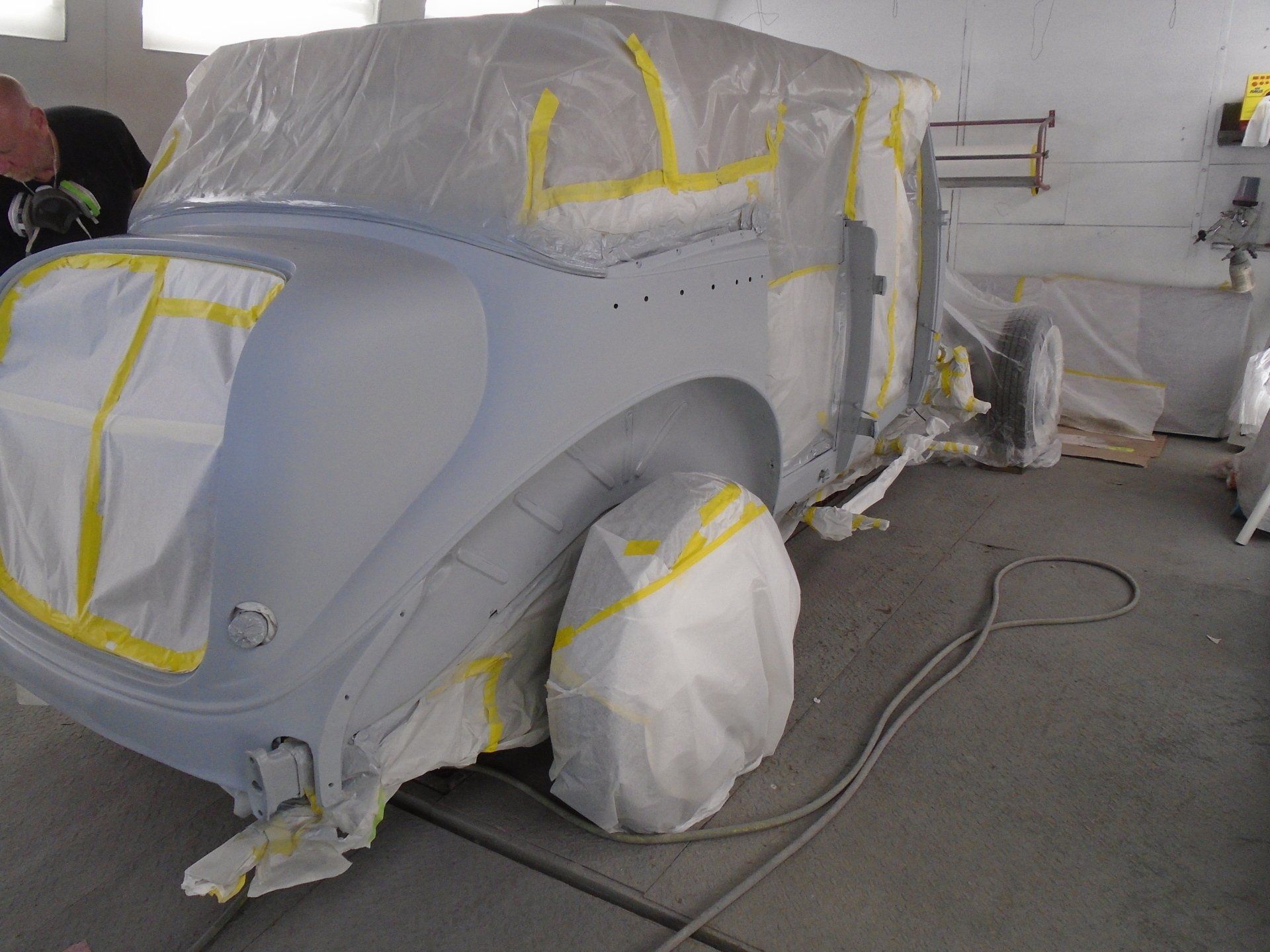 Car prepared for painting in a garage, taped and covered in plastic.