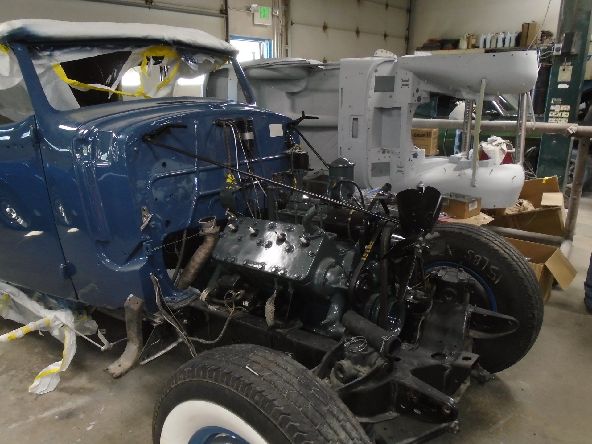 Blue vintage car being restored in a shop; engine visible; body parts in the background.