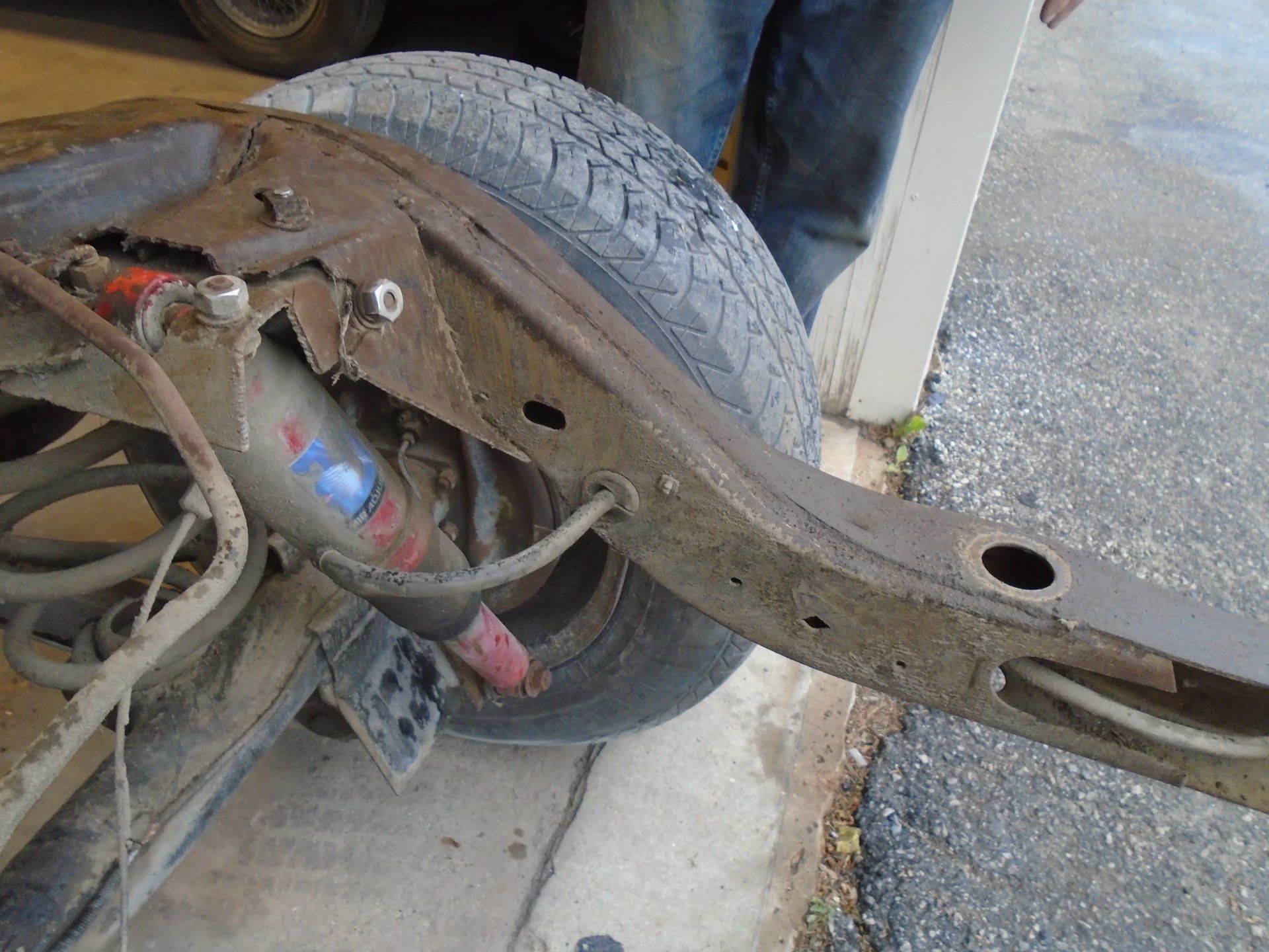Rusty car frame with a tire, shock absorber, and suspension components.