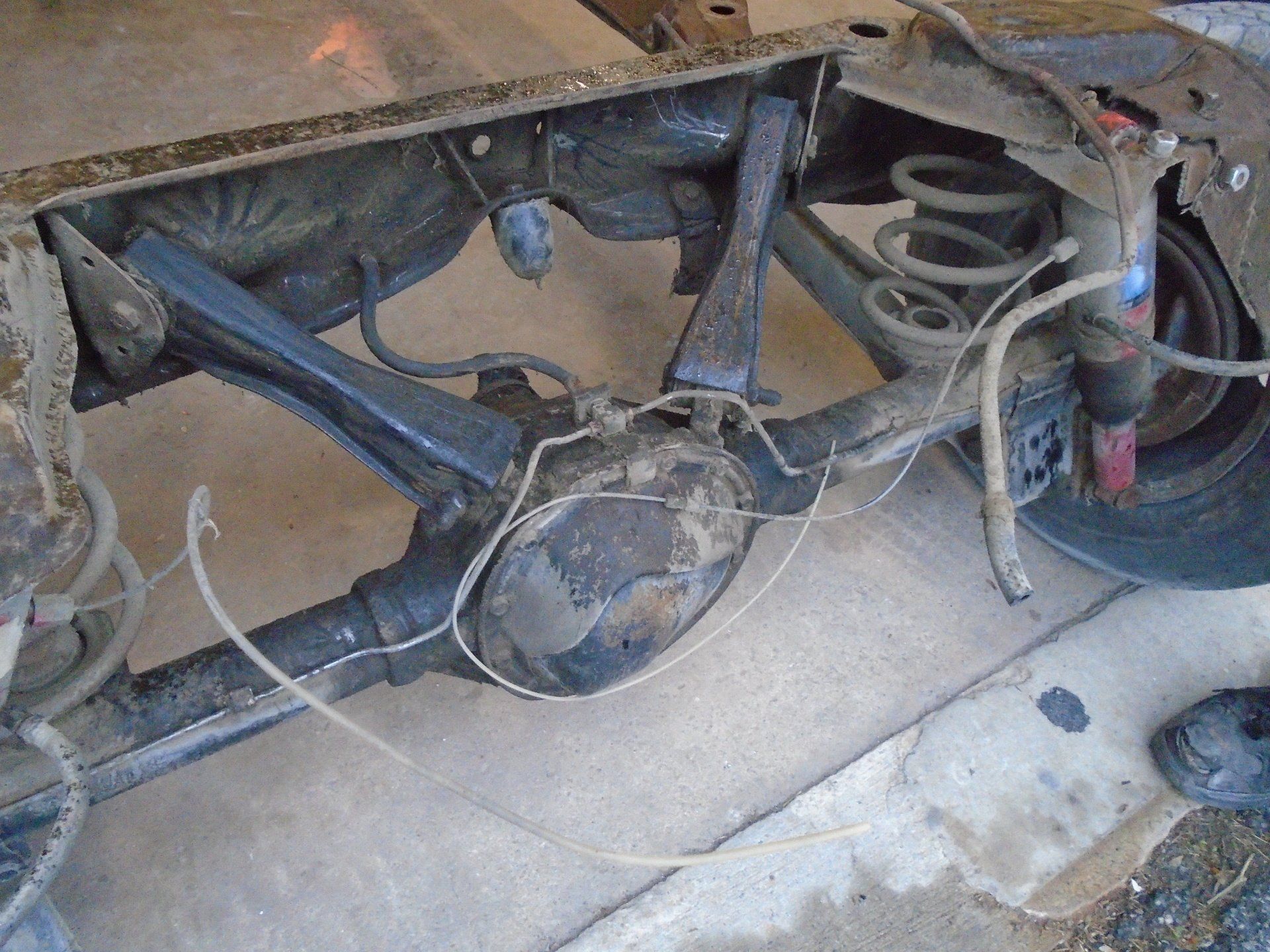 Rear axle assembly from a vehicle, with suspension components visible, in a garage setting.